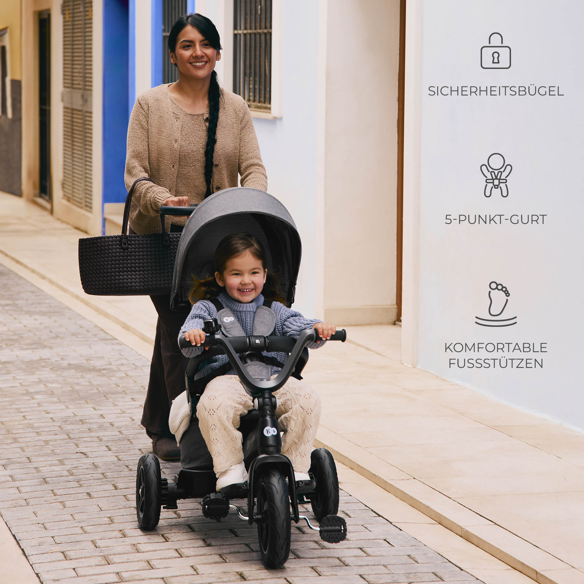 Eine Frau schiebt ein Kind in einem Dreirad mit Verdeck durch eine Gasse.