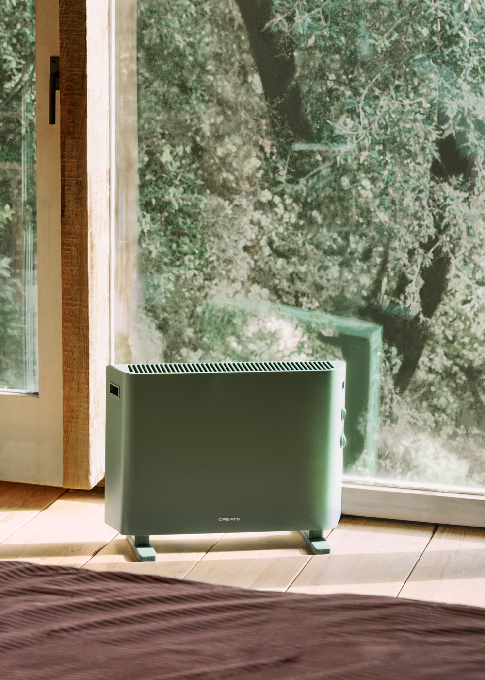 Un radiador verde está sobre un suelo de madera frente a una ventana con follaje verde.