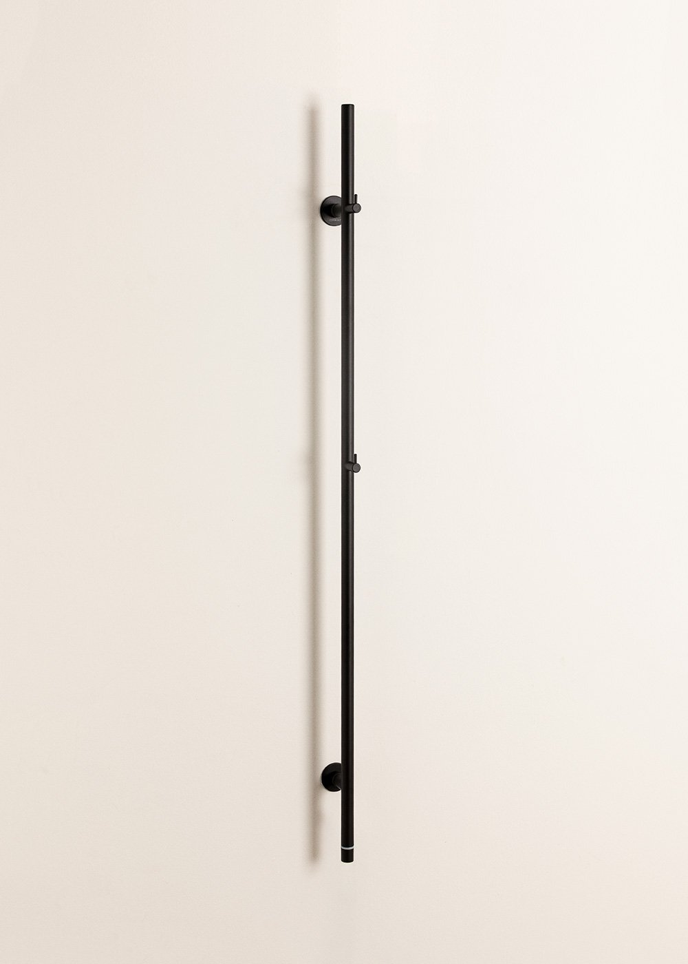 Un tirador de barra vertical negro con dos puntos de montaje en una pared color crema.