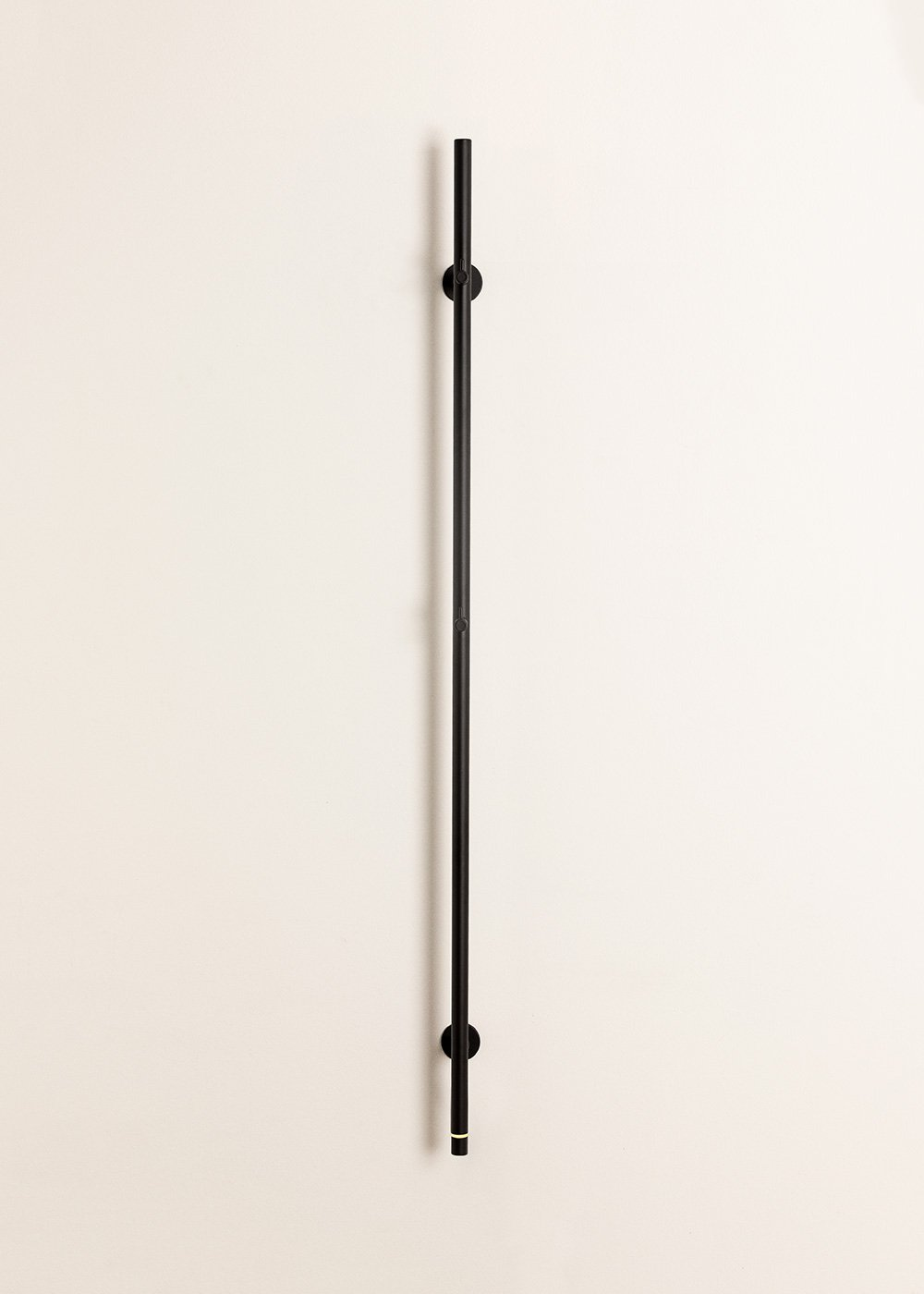 Un asa vertical negra con dos soportes en una pared color crema.