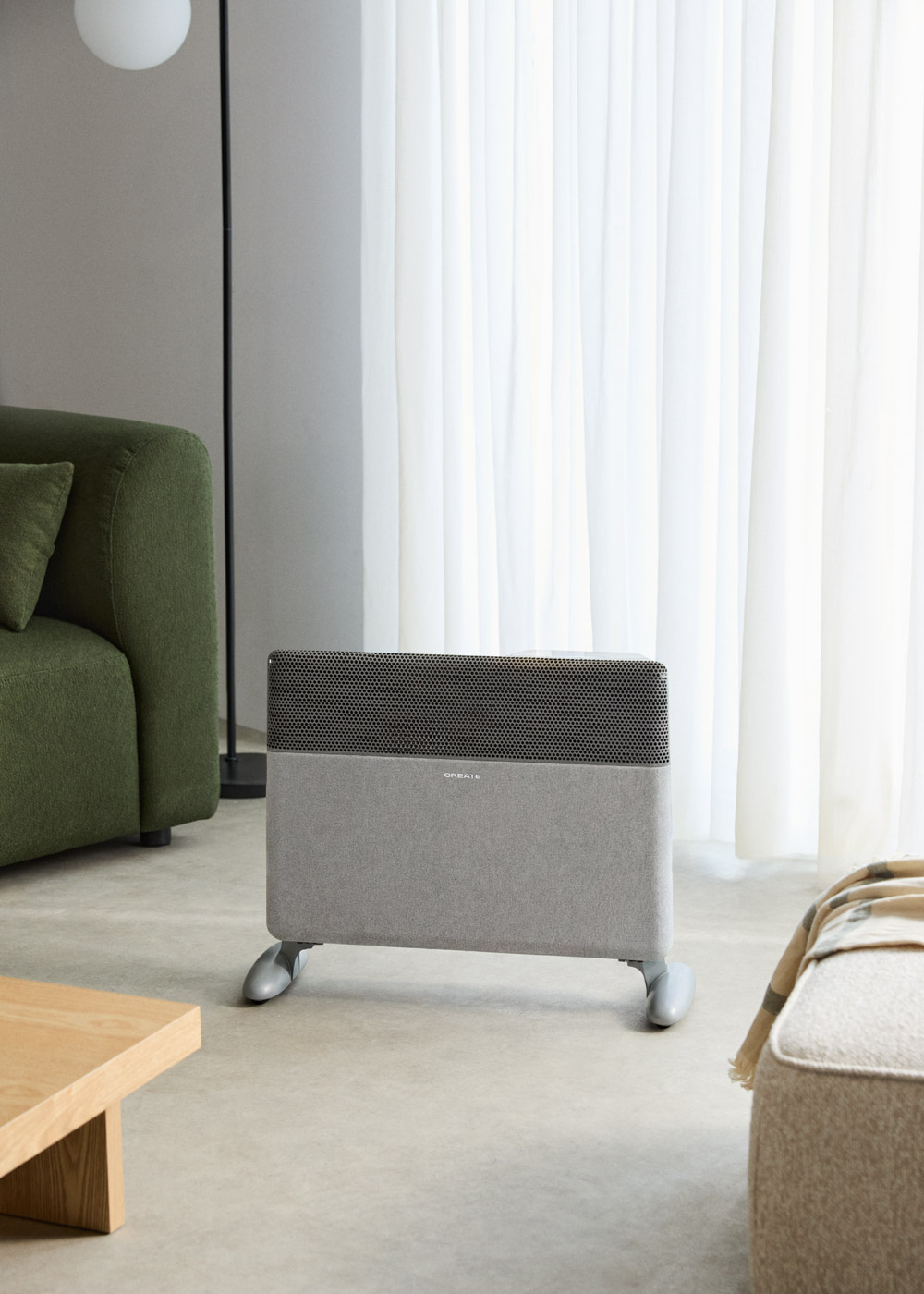 Un radiador gris con rejilla de ventilación junto a un sofá verde.