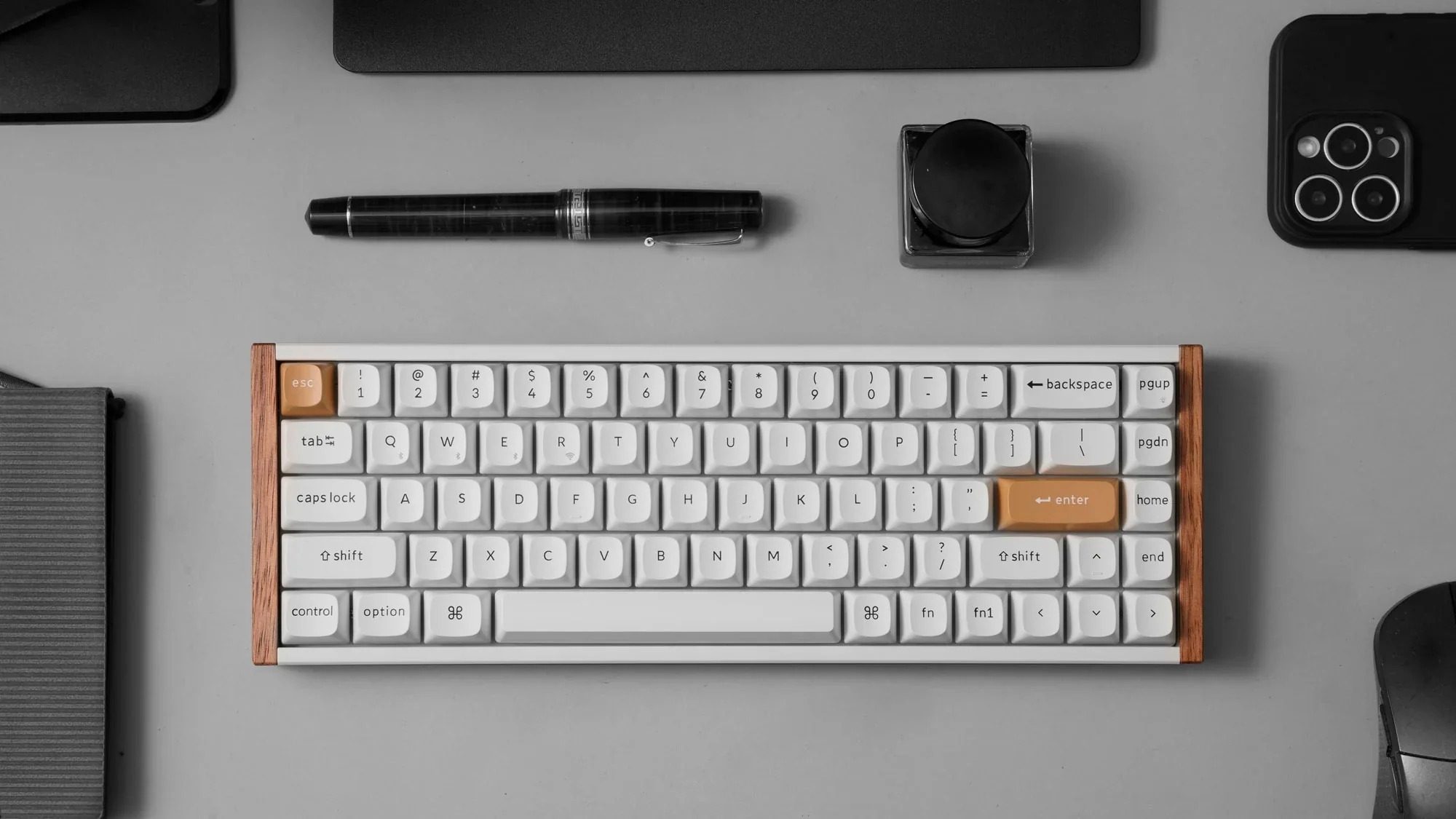 Biała klawiatura mechaniczna z drewnianym wykończeniem leży na szarej powierzchni z akcesoriami biurkowymi.