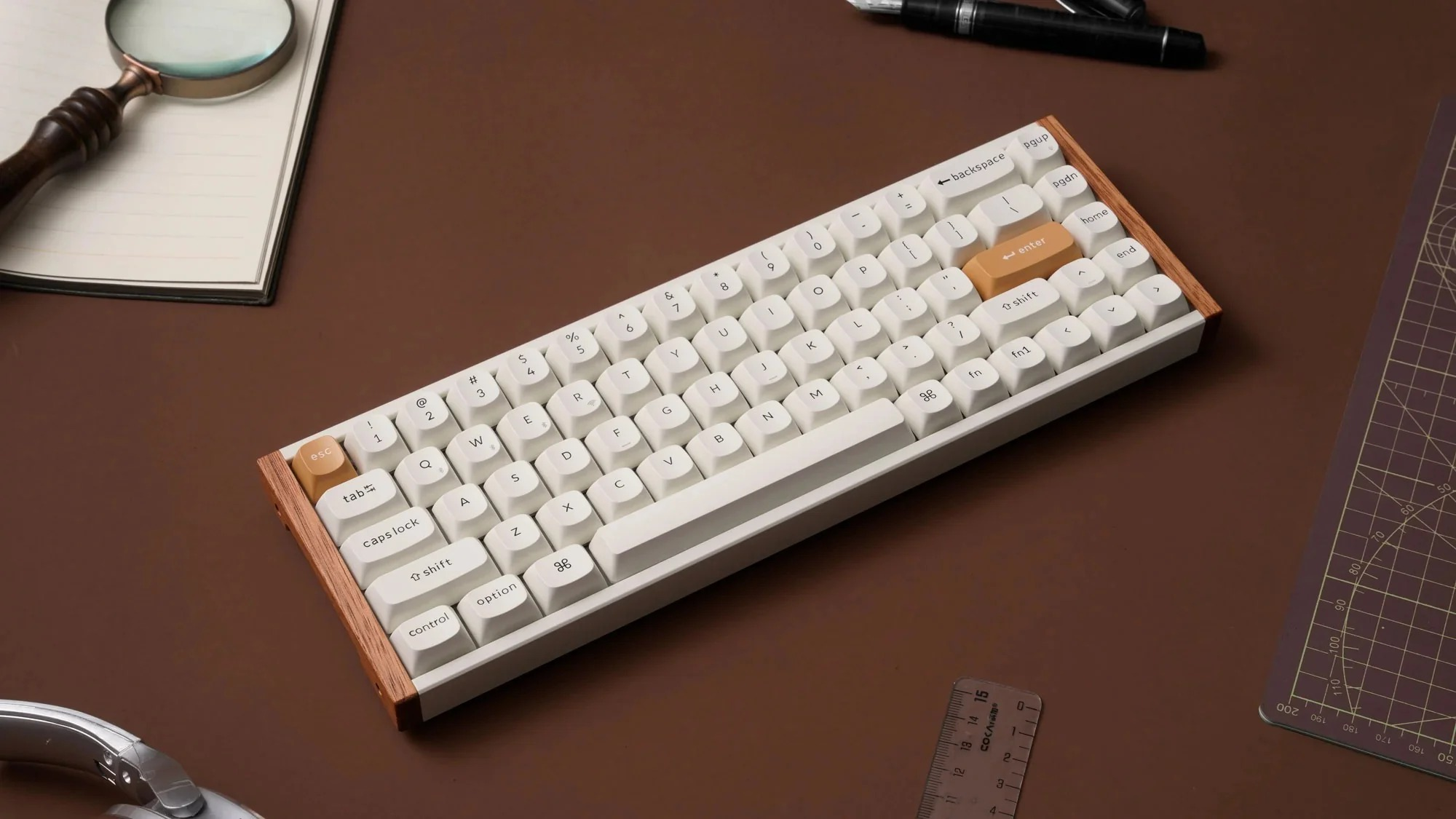 Biała klawiatura mechaniczna z drewnianą ramką na brązowym biurku, z notatnikiem, lupą i linijką.