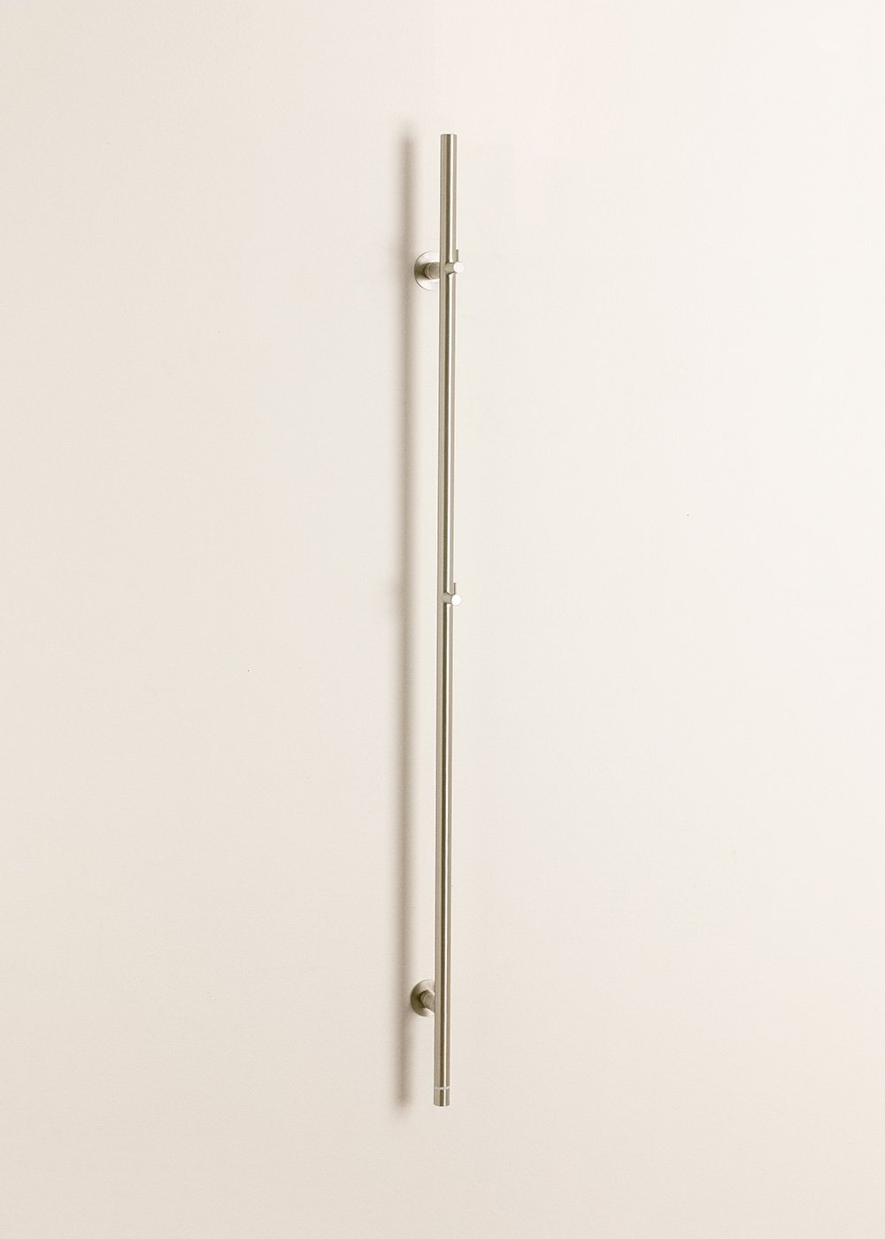 Un tirador largo y delgado de plata está montado verticalmente en una pared color crema.