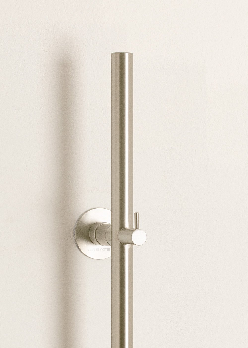 Un soporte plateado para alcachofa de ducha con barra vertical y gancho en la pared.
