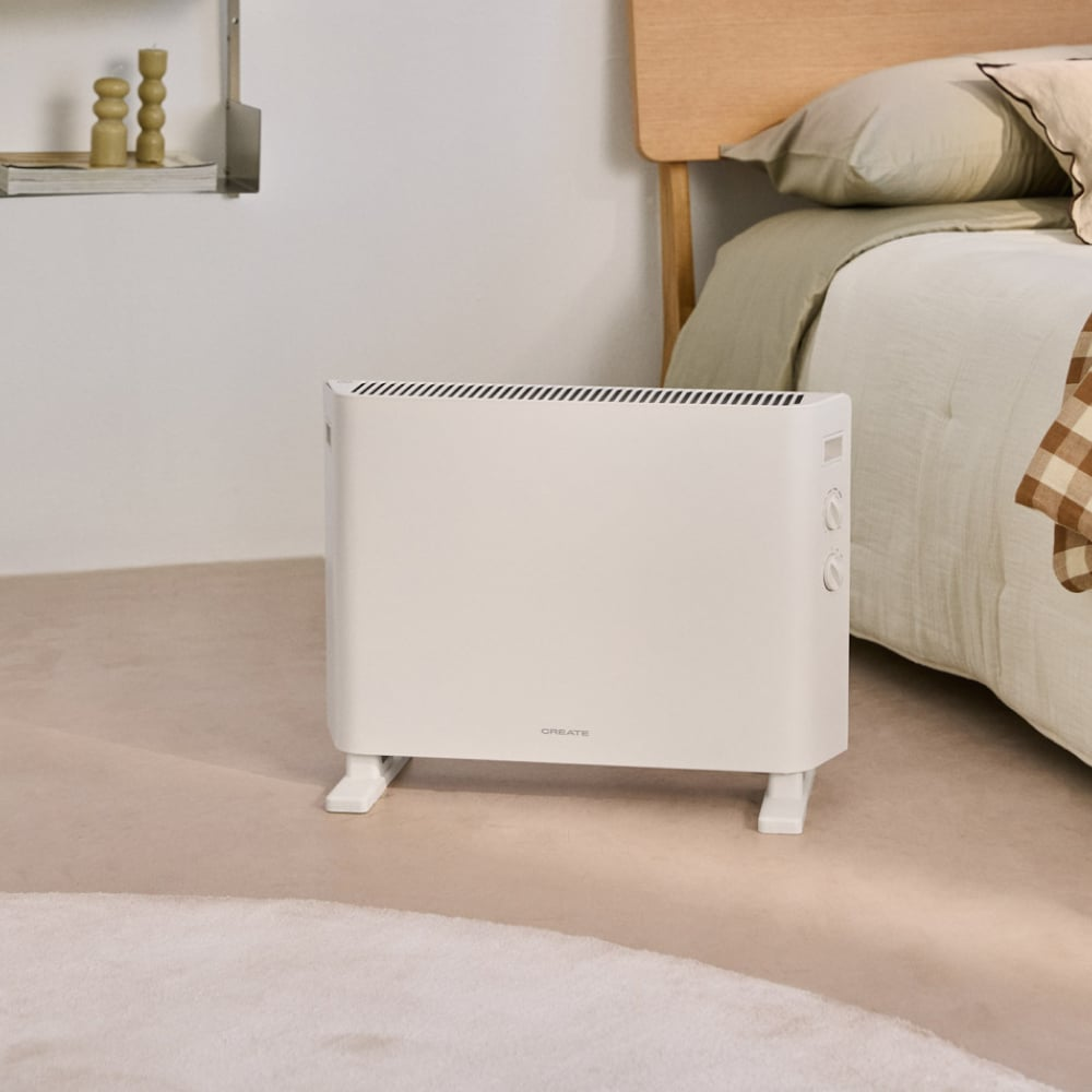 Un radiador blanco está en el suelo junto a una cama con ropa de cama.