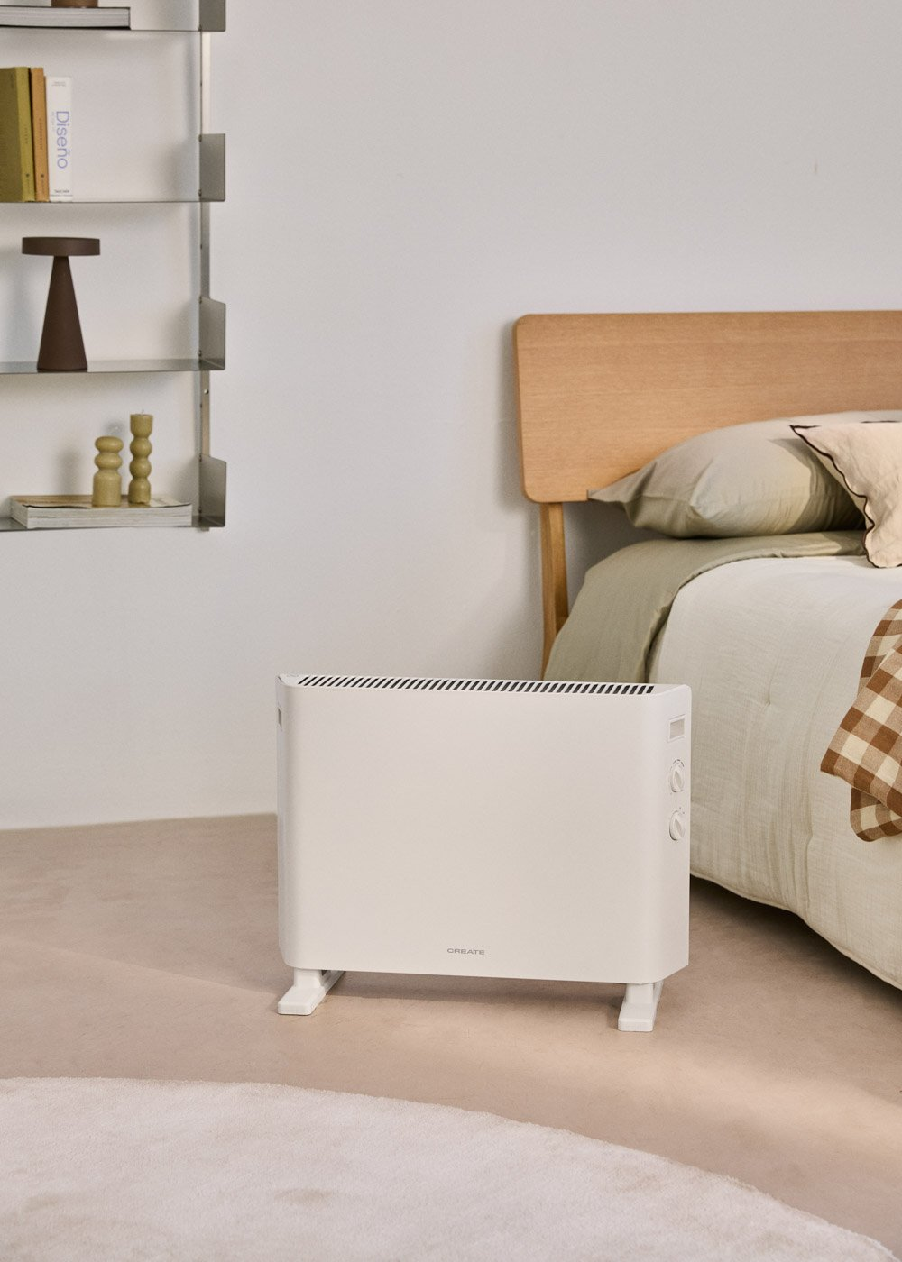 Un radiador blanco está junto a una cama con manta de cuadros marrones.