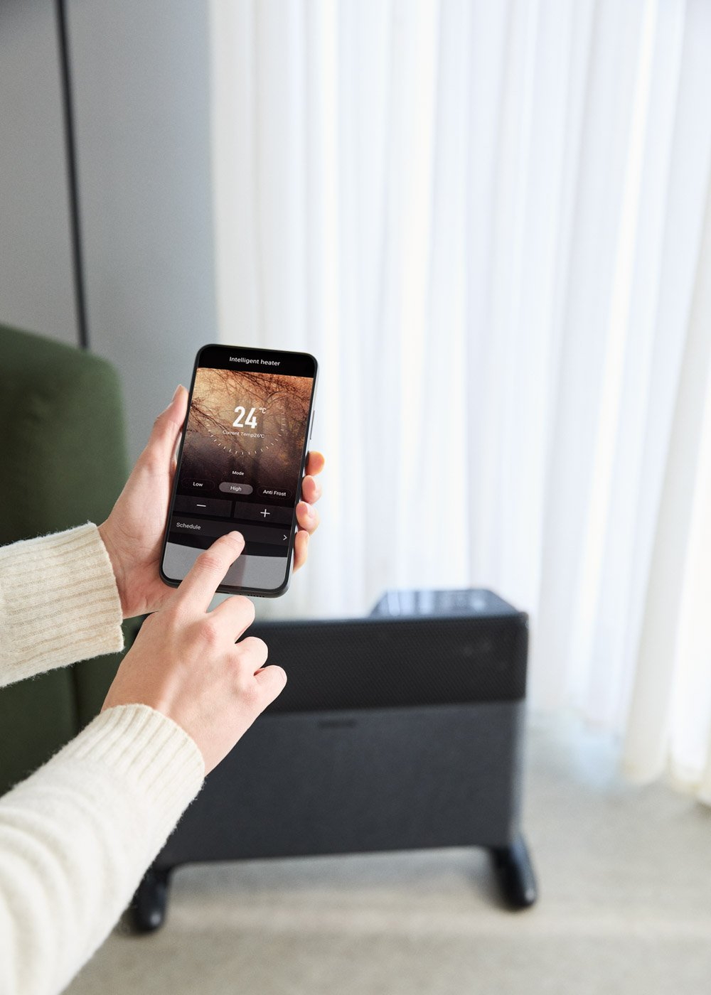 Una persona usa un smartphone para operar un calentador oscuro con controles.