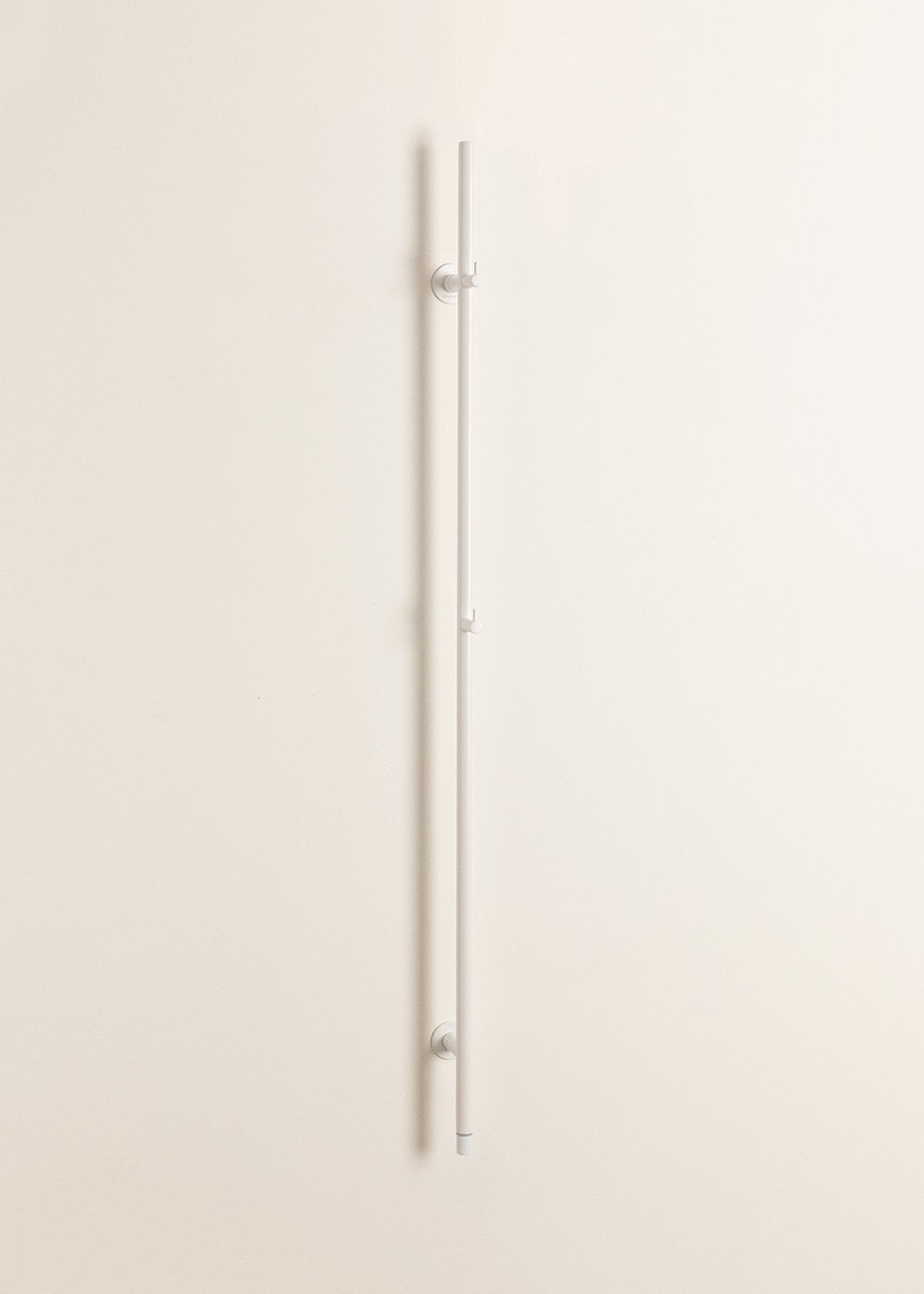 Una percha larga y delgada blanca cuelga verticalmente en una pared beige.