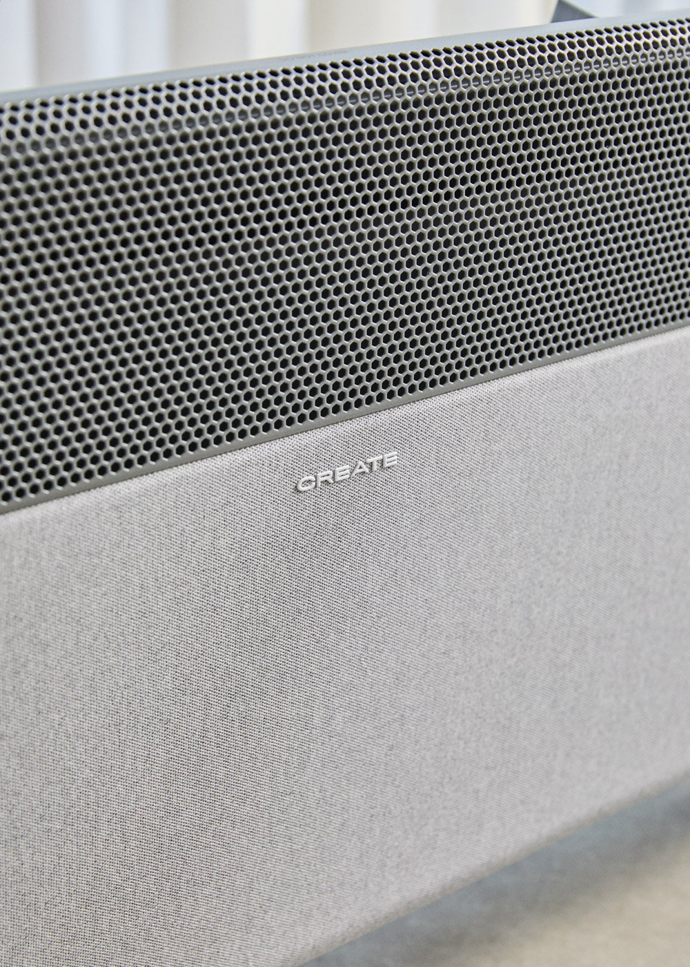 Altavoz gris con rejilla perforada y cubierta de tela. La palabra CREATE está en relieve.