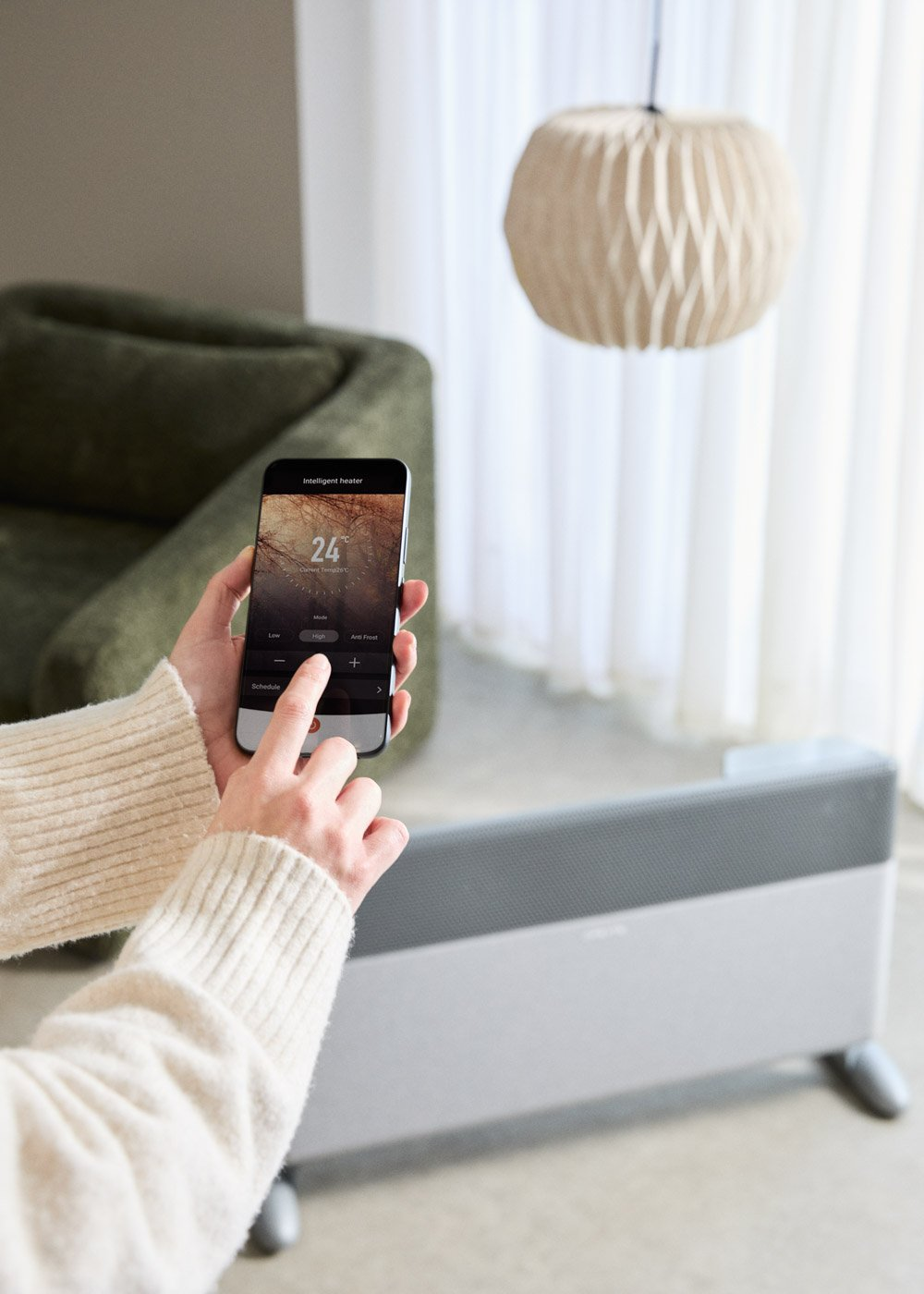 Manos sujetando smartphone con controles de calefacción. Un radiador a la derecha.