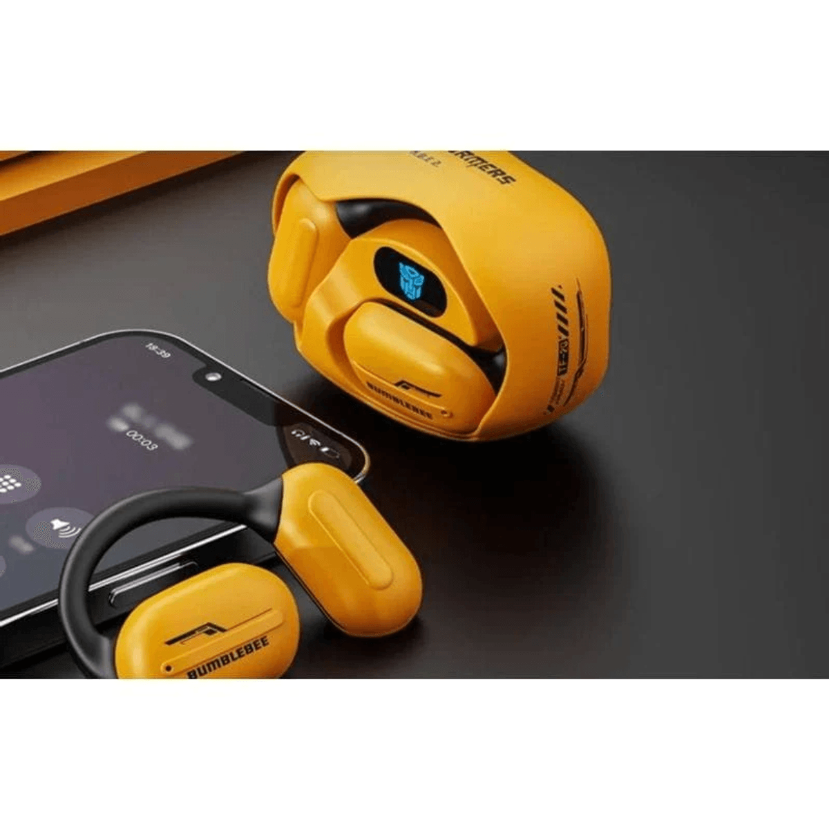Un juego de auriculares Bumblebee amarillo con estuche de carga y smartphone.