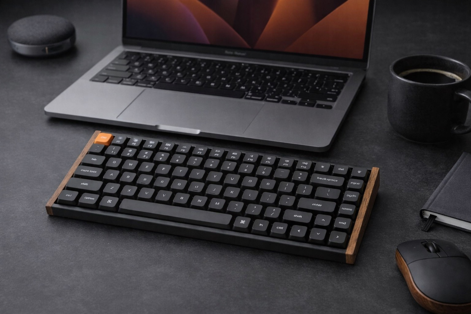 Laptop, klawiatura z drewnianą ramką, mysz i kubek kawy na ciemnym biurku.