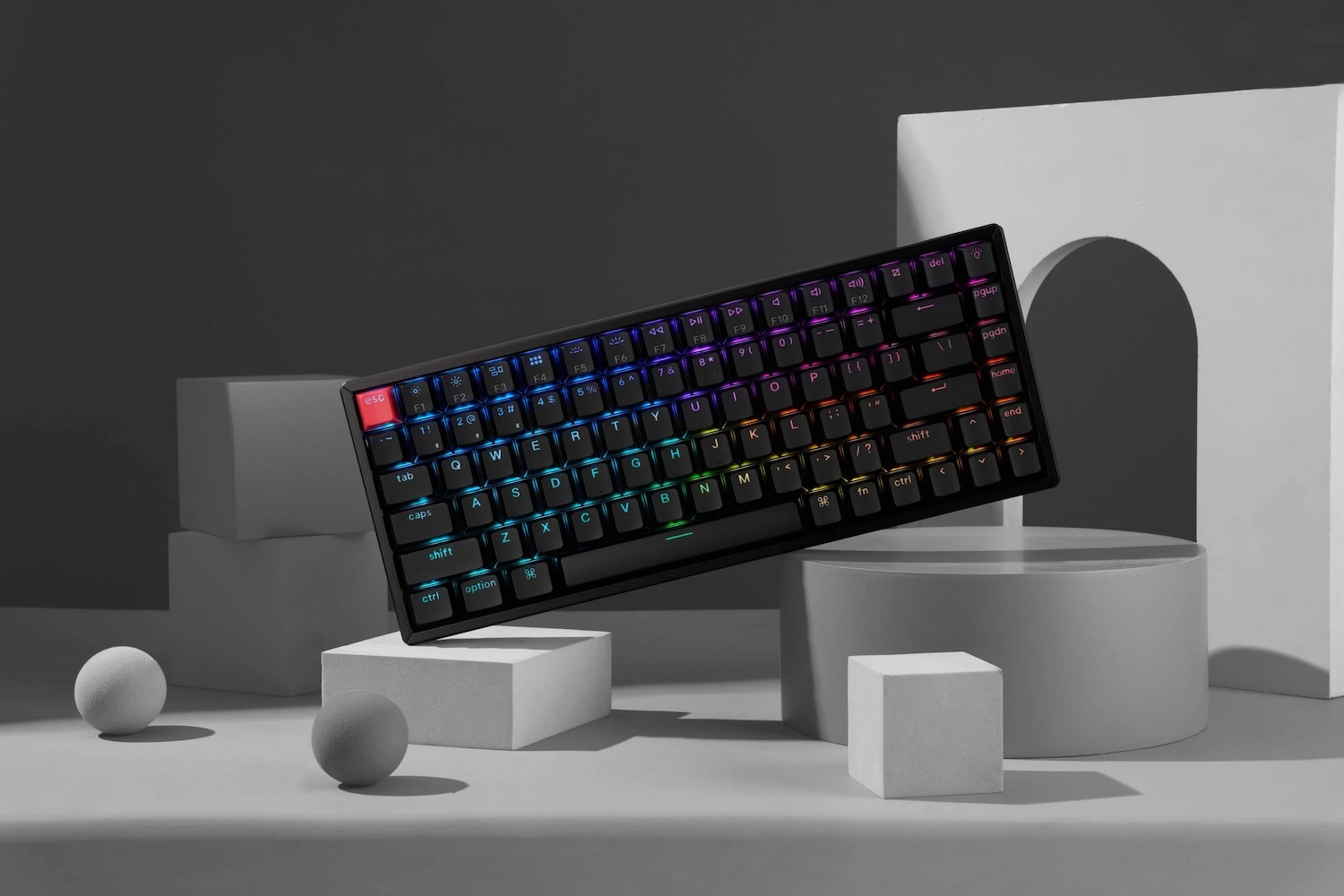 Czarna klawiatura z podświetleniem RGB stoi na ekspozycji z geometrycznymi kształtami.