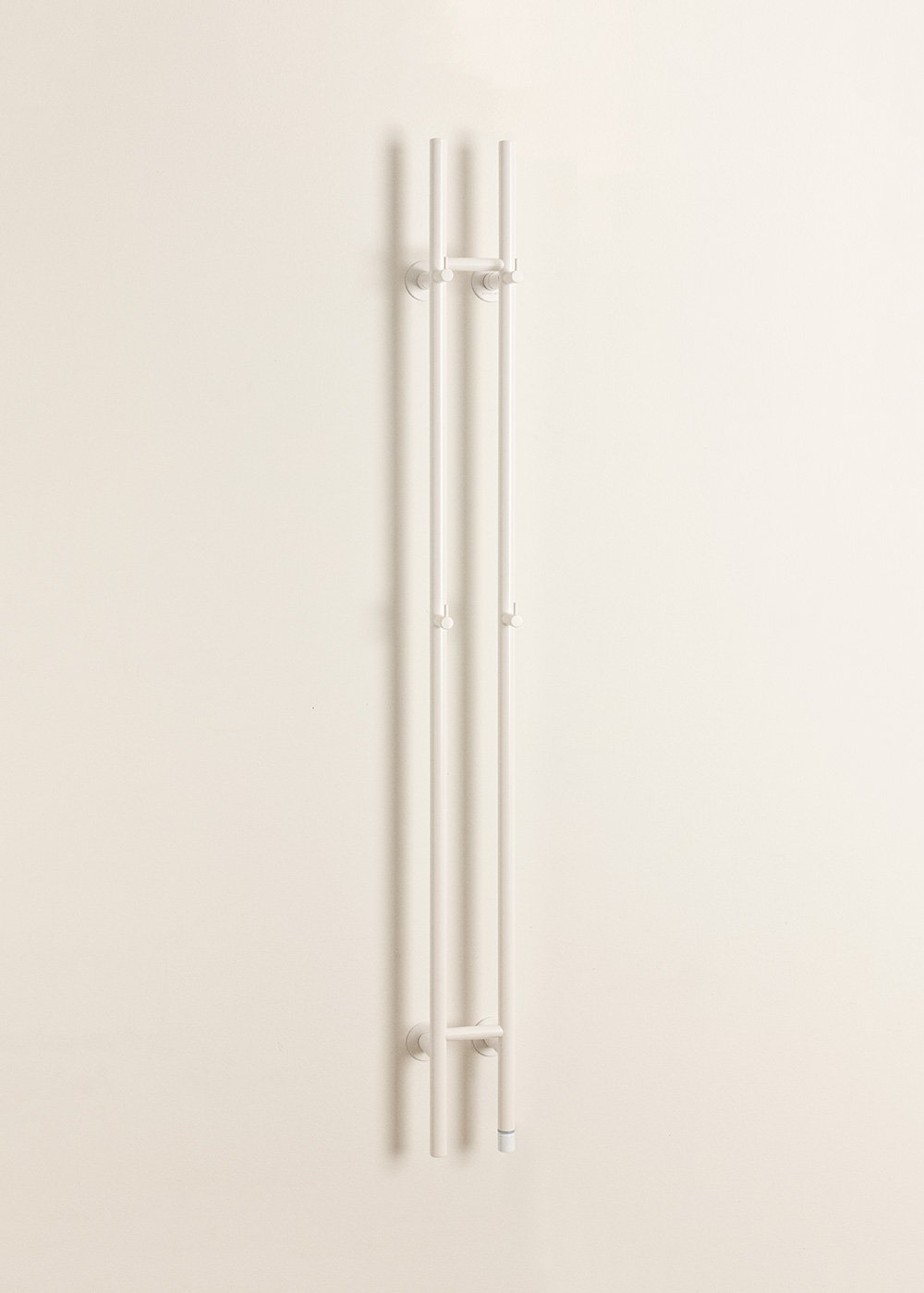 Un radiador blanco con tres tubos verticales, montado en una pared color crema.