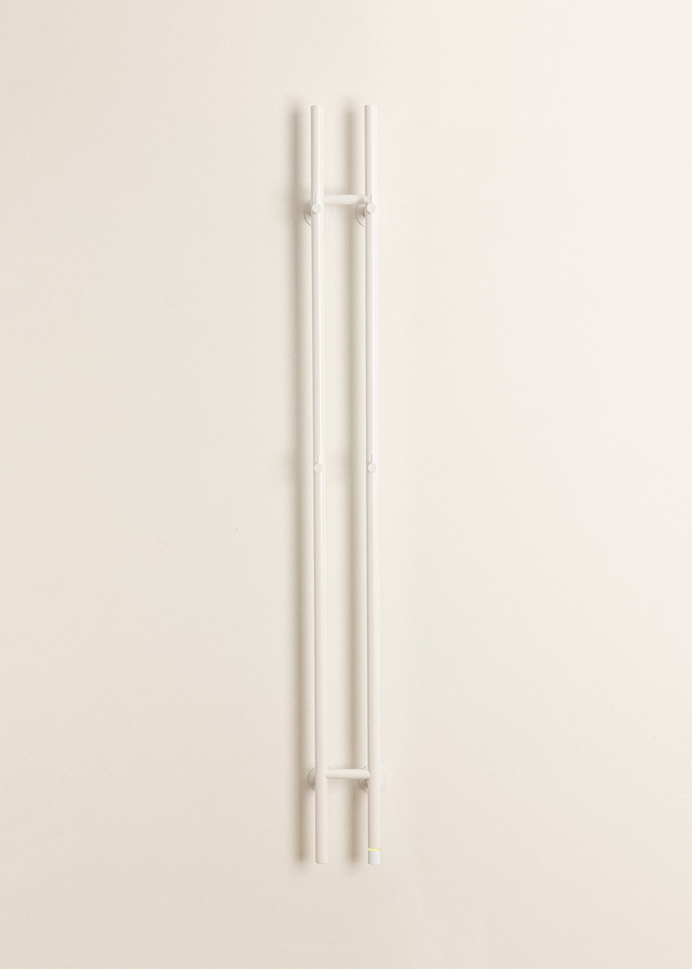 Un objeto blanco en forma de H hecho de tubos de metal, colgado en una pared color crema.