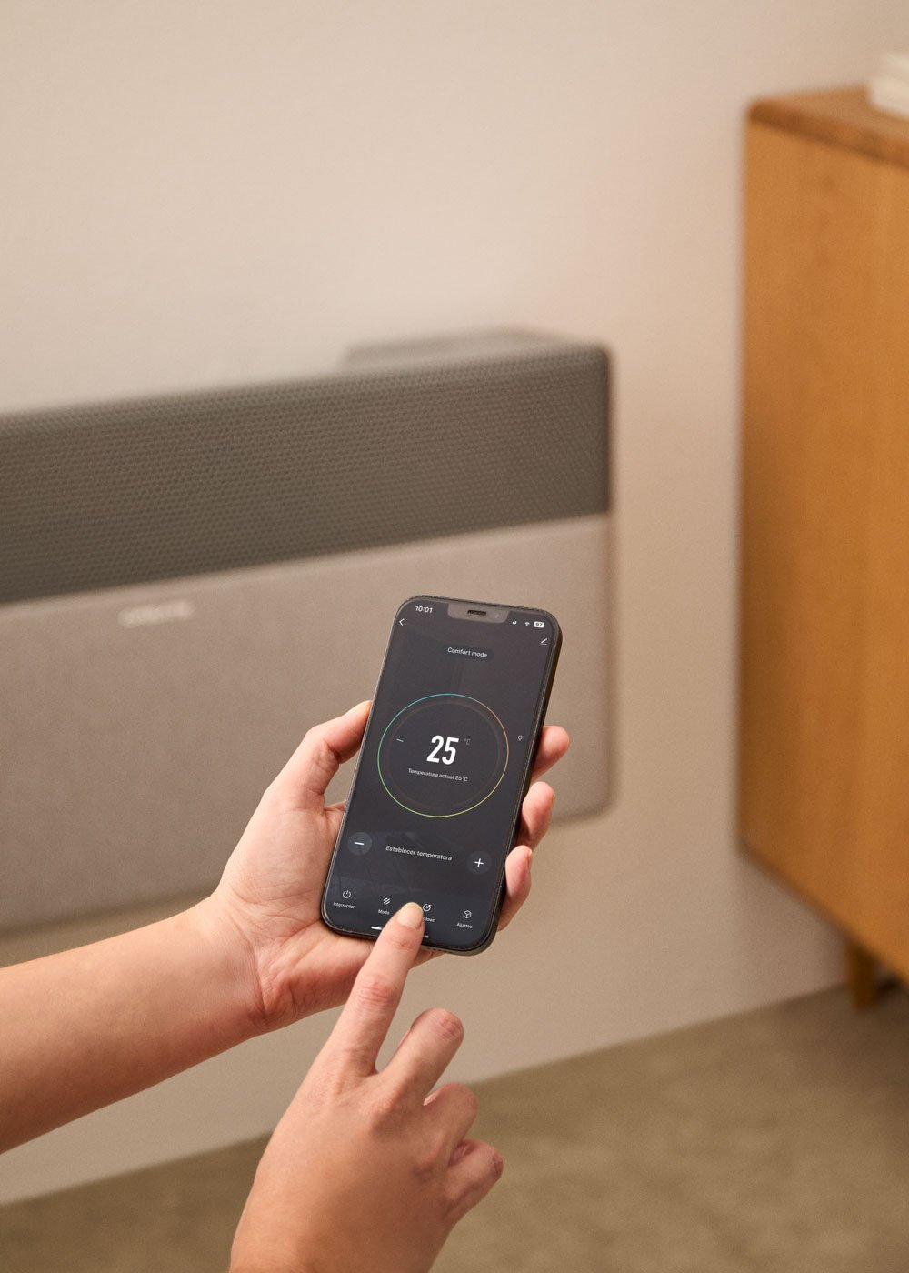 Mano sostiene smartphone con control de calefacción, 25°C mostrados, radiador al fondo.