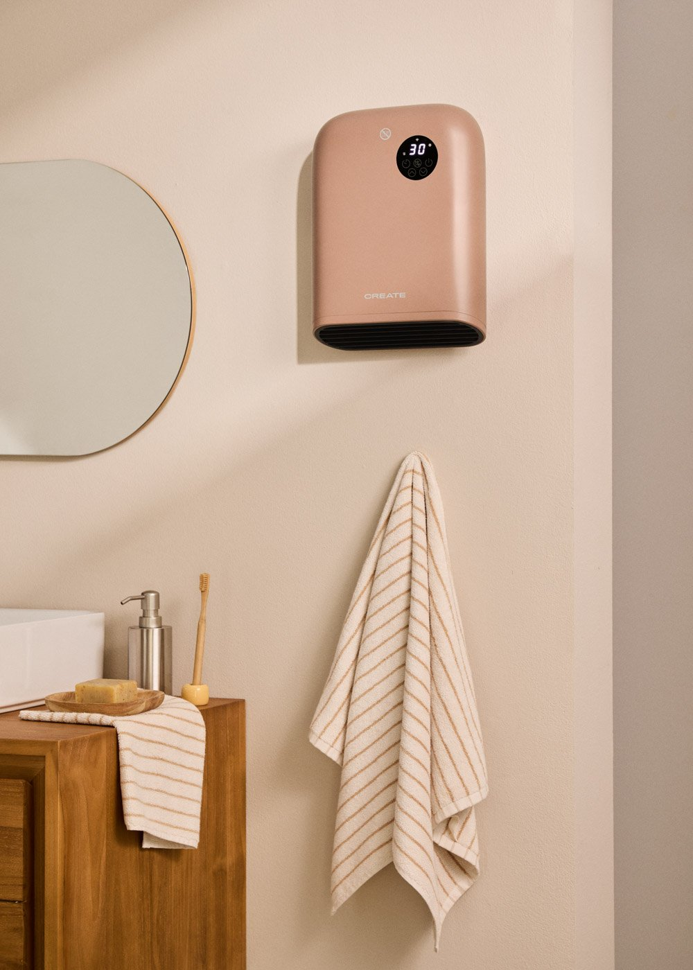 Un calentador de baño rosa cuelga en la pared junto a un espejo y un mueble de madera con jabón.