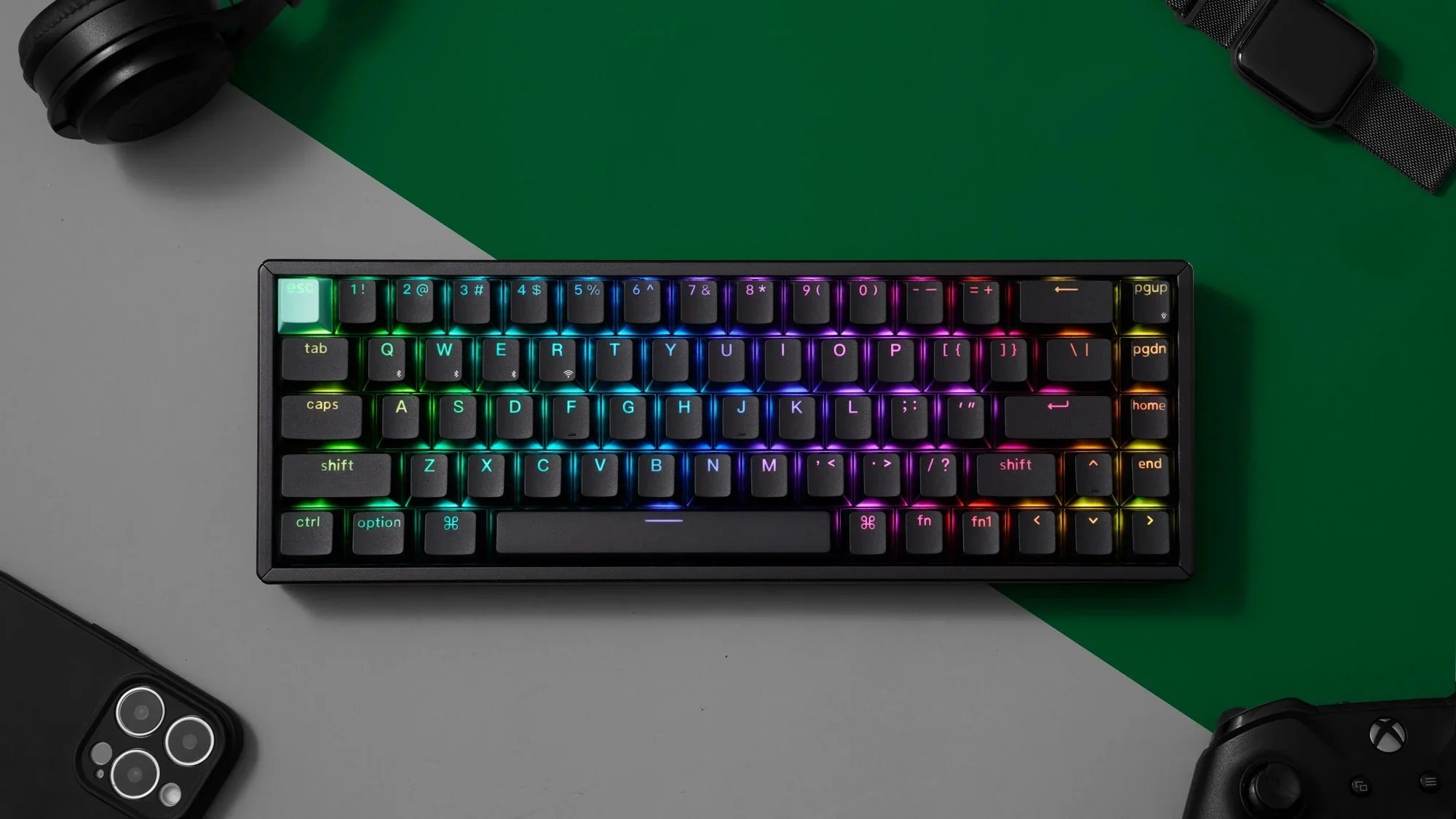 Czarna klawiatura mechaniczna z podświetleniem RGB, słuchawkami, smartwatchem i telefonem.