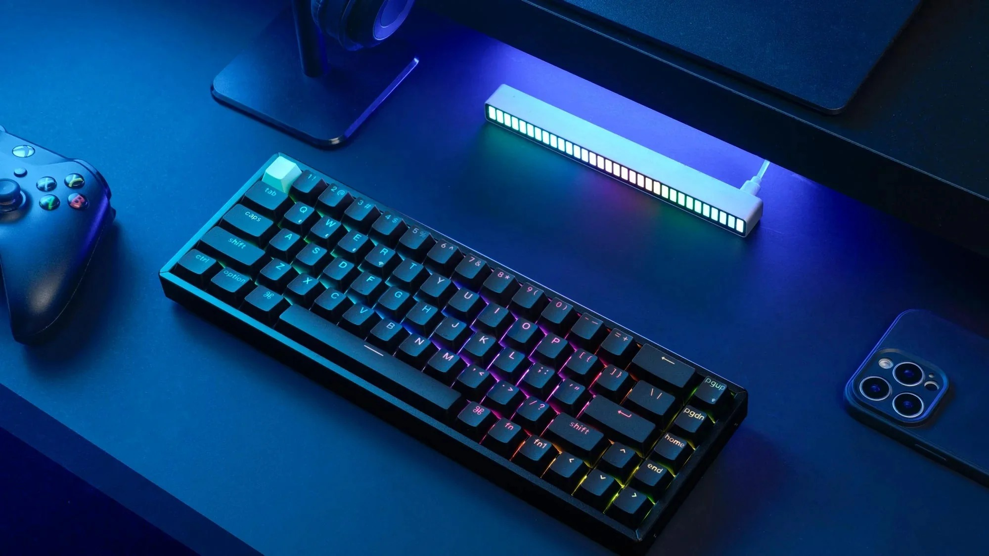 Klawiatura gamingowa, kontroler i smartfon na niebieskim biurku.