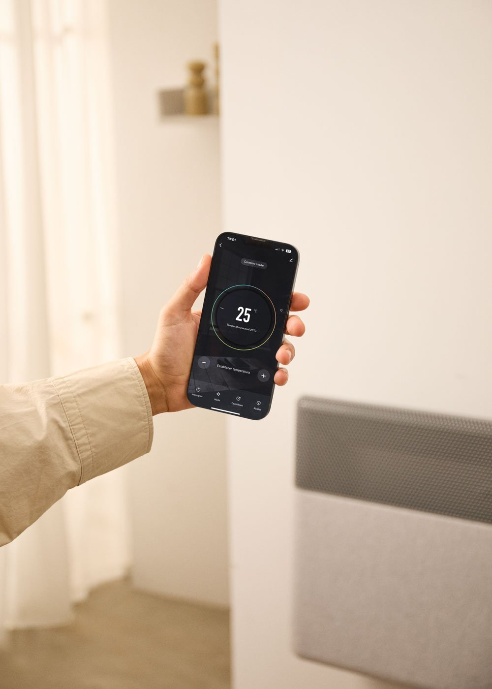 Una mano sostiene un smartphone que muestra una app de control de calefacción con 25°C.