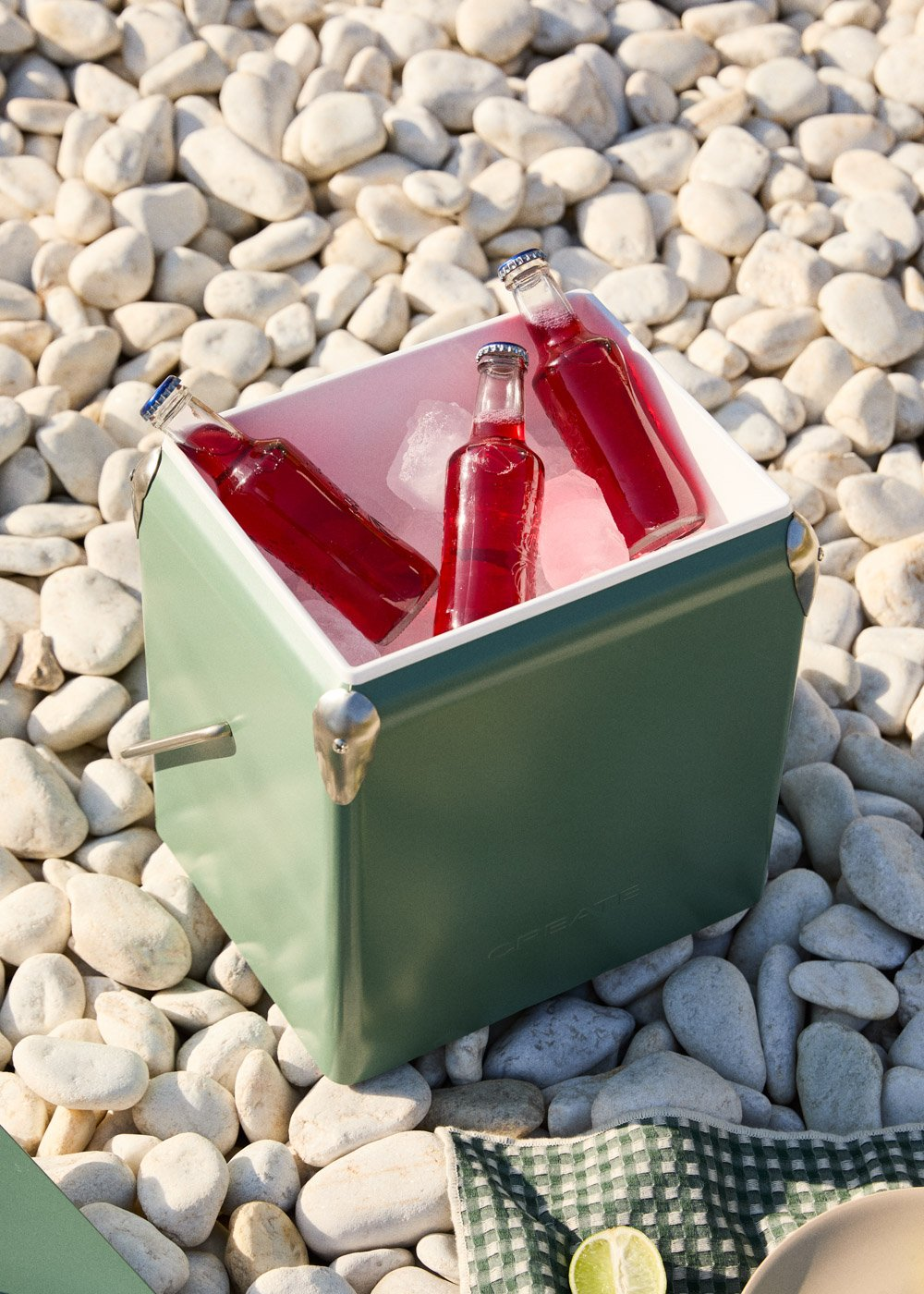 Nevera verde con tres botellas rojas y hielo sobre guijarros.