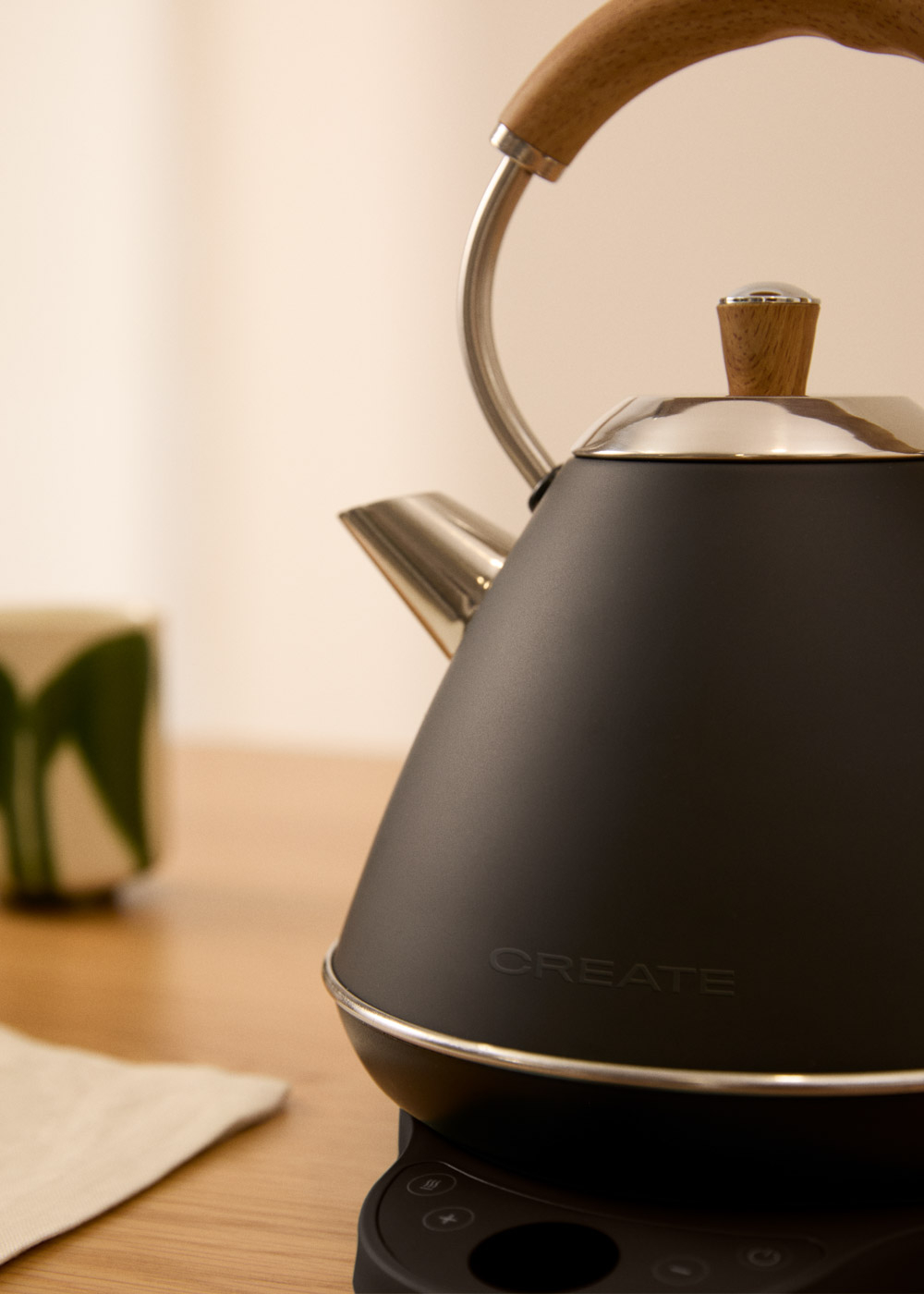 Tetera negra con mango de madera sobre base negra, junto a una taza.
