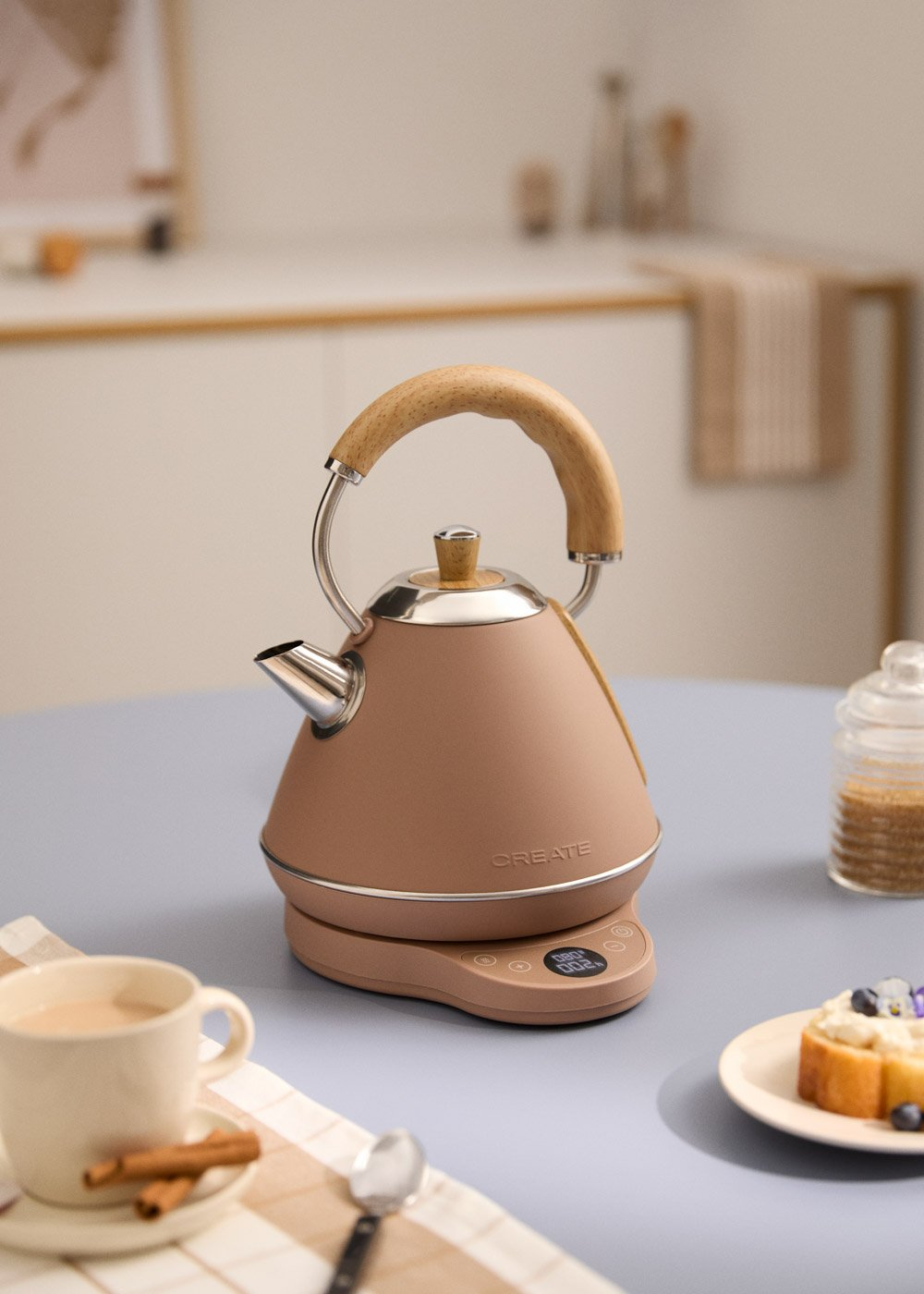 Una tetera marrón con asa de madera sobre una báscula junto a una taza de té y un pastel.