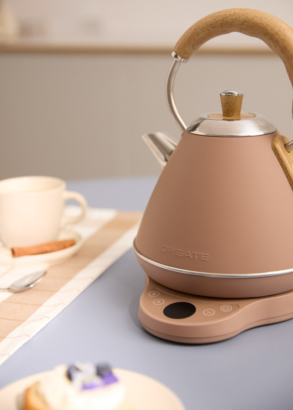 Una tetera marrón con asa de madera sobre una báscula. Cerca hay una taza y una cuchara.