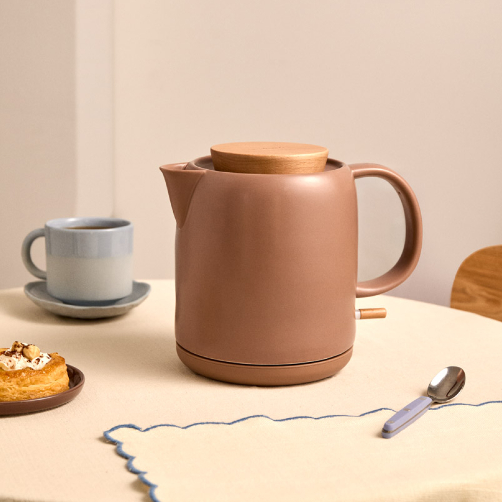 Una tetera marrón con tapa de madera sobre una mesa con un pastel y una taza.