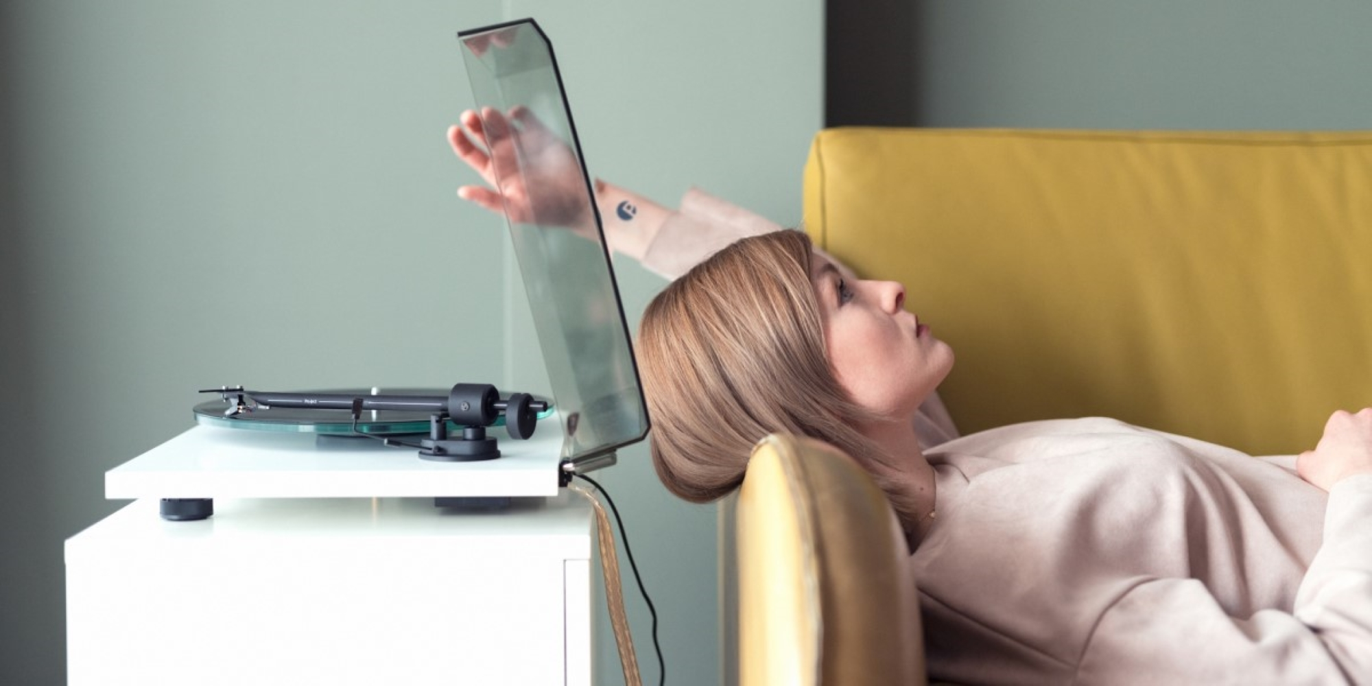 Kobieta leży na żółtej sofie obok gramofonu.