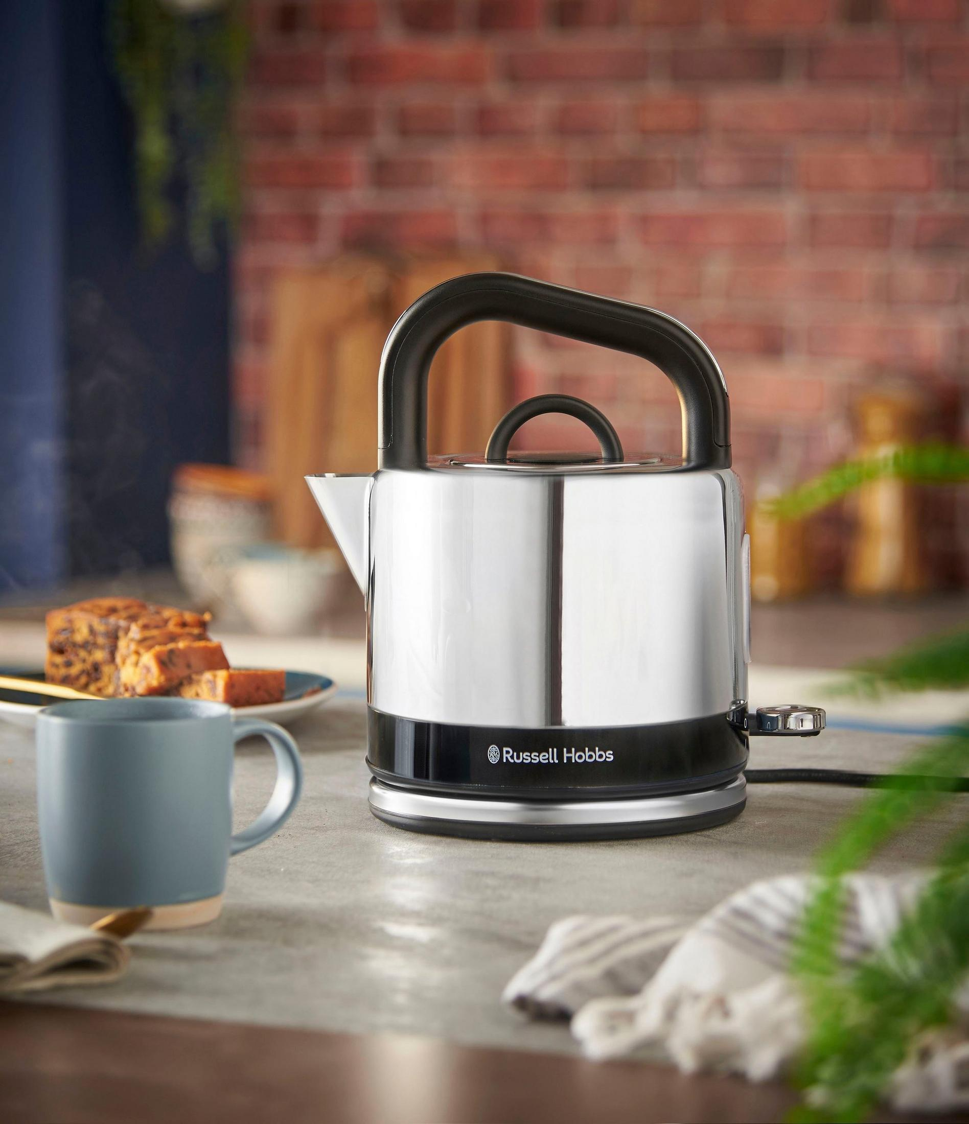 Ein glänzender Russell Hobbs Wasserkocher dampft neben einer Tasse und einem Obstkuchen auf einer Arbeitsplatte.