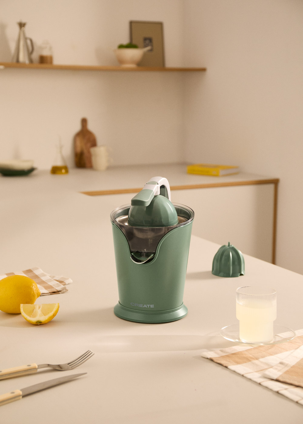 Un exprimidor de cítricos verde está sobre una mesa junto a limones y un vaso de jugo.