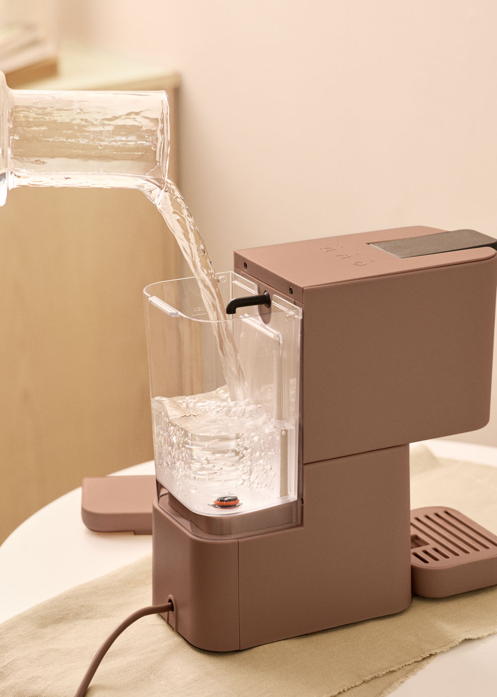 Se vierte agua de una jarra de vidrio en el depósito de agua de una cafetera.