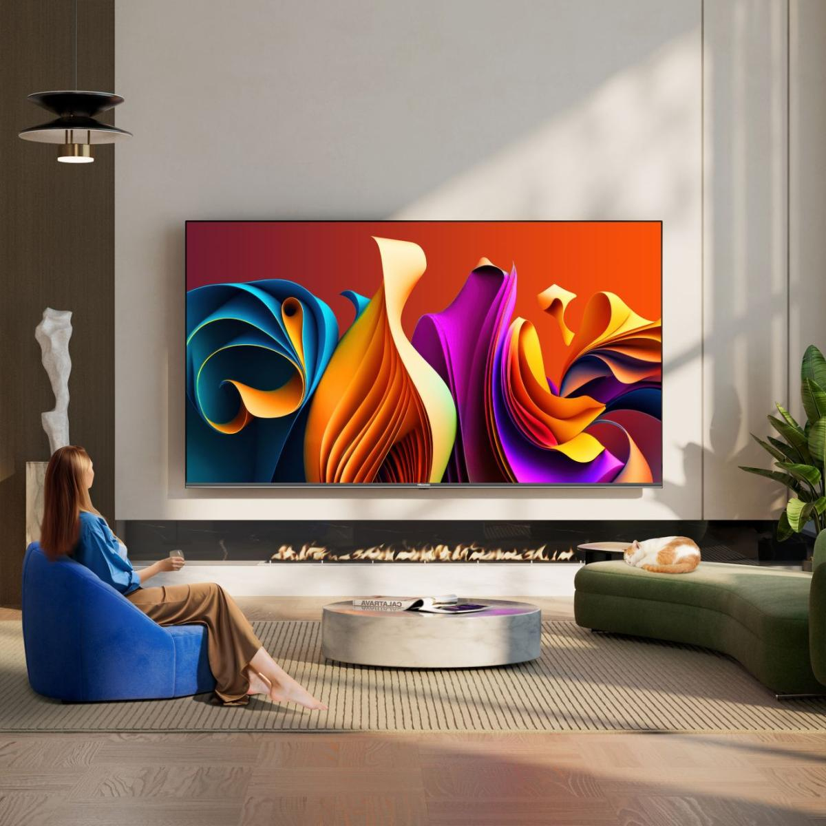 Una donna seduta su una poltrona blu guarda un grande TV con arte astratta.