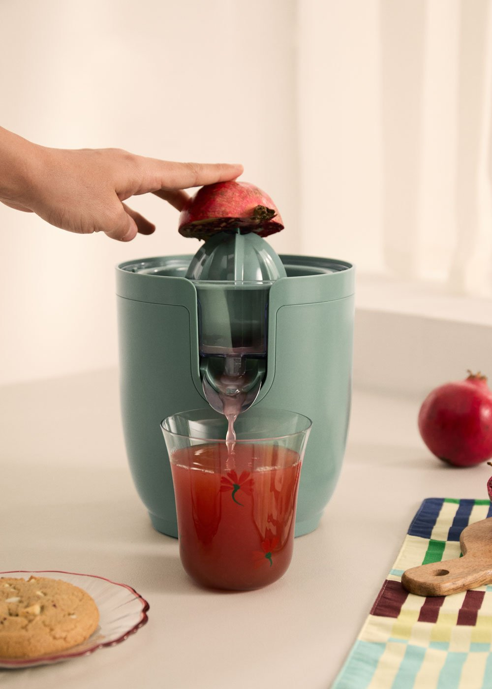 Una mano presiona una granada en un exprimidor, el jugo fluye hacia un vaso.