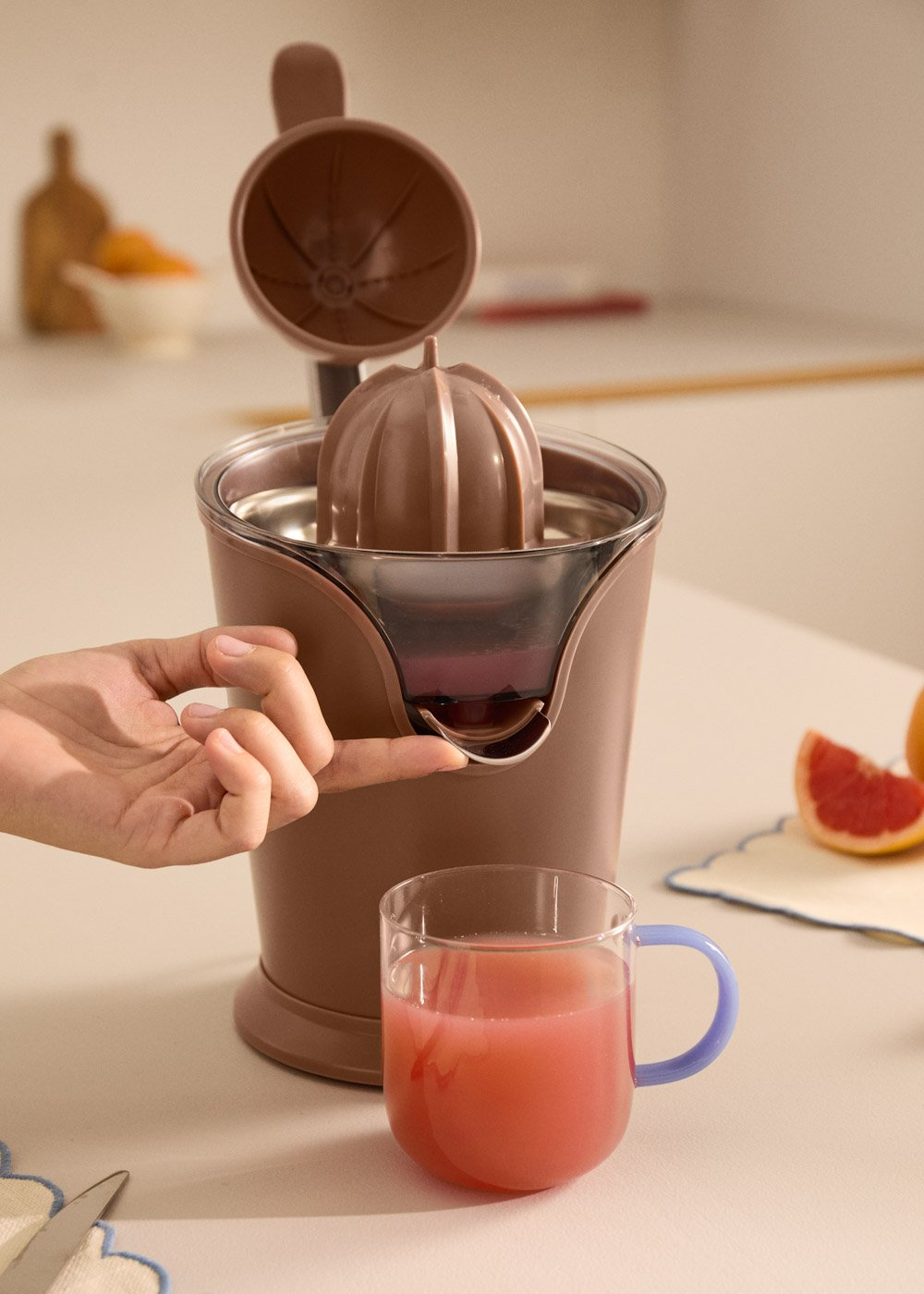 Una mano presiona una licuadora, con un vaso de jugo al lado.