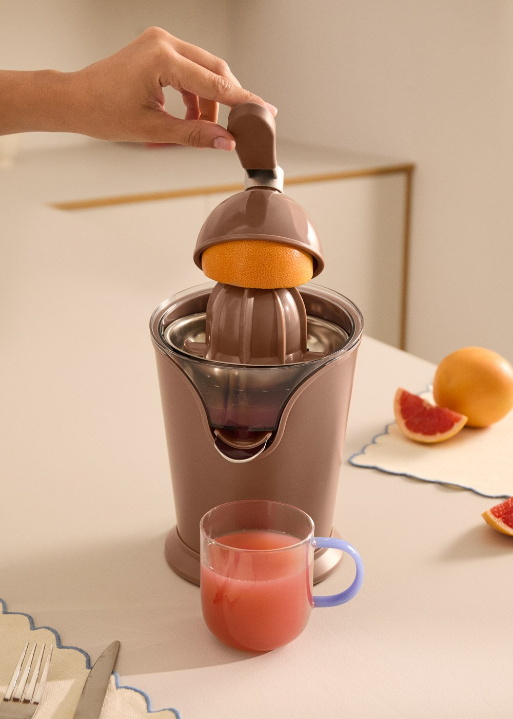 Una mano presiona un exprimidor de pomelos, con fruta y zumo cerca.