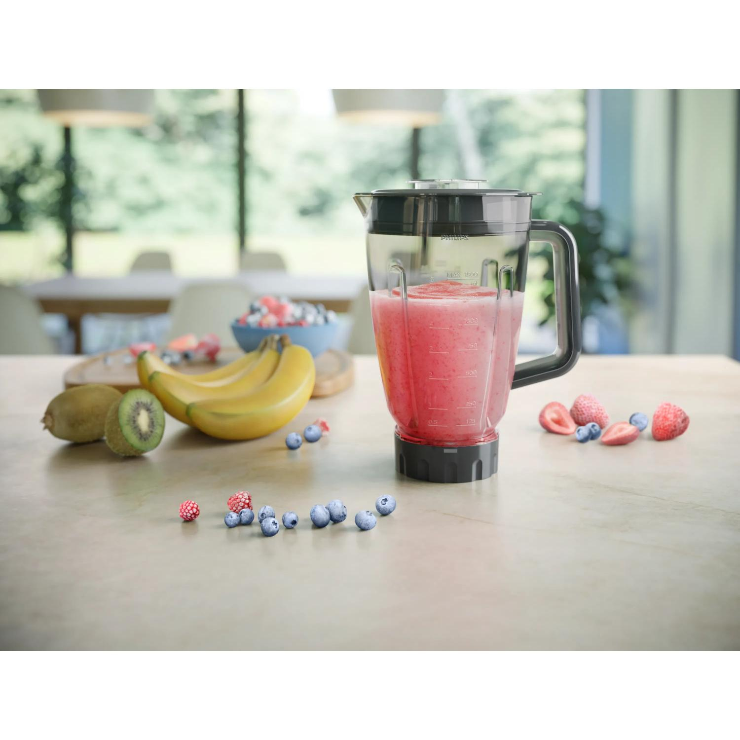 Blender z czerwonym smoothie stoi na blacie z owocami.
