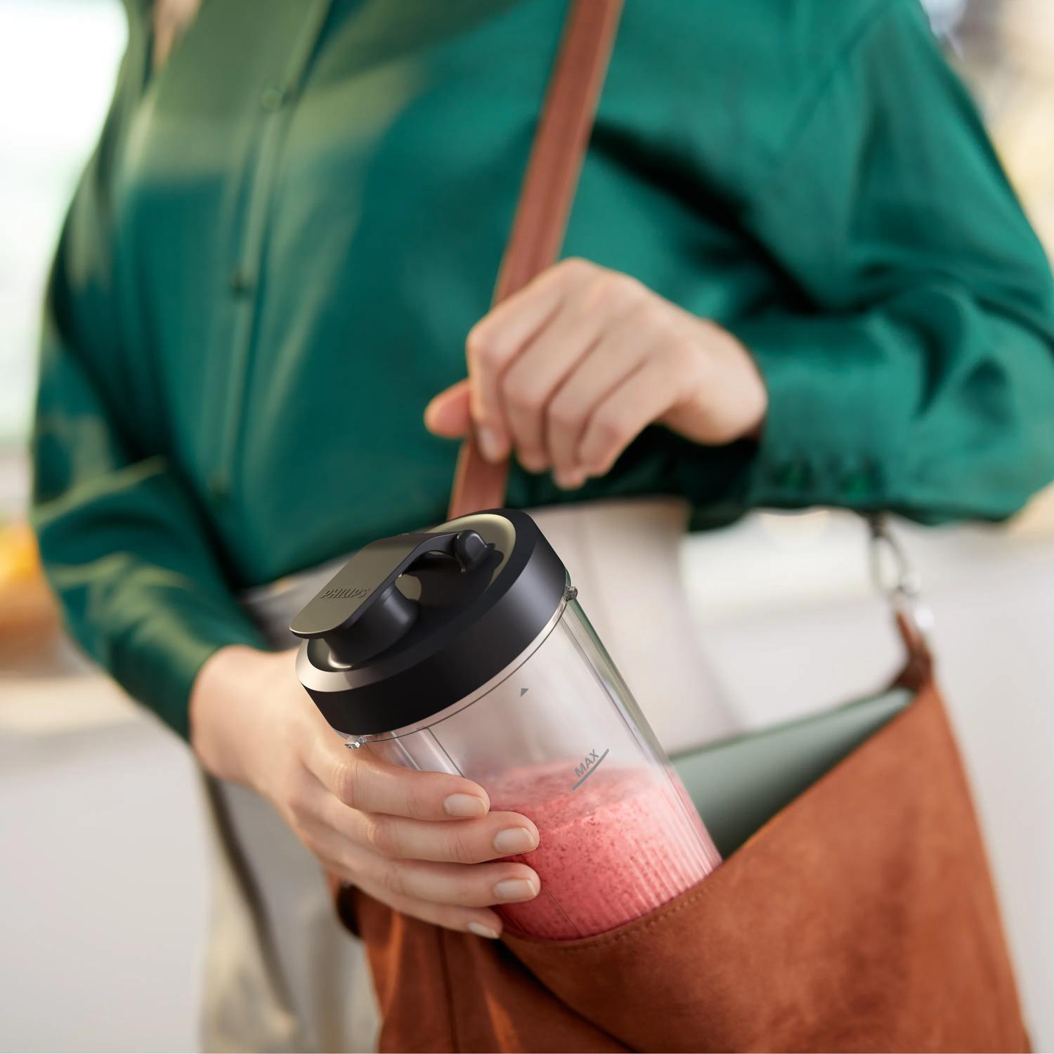 Osoba wkłada przezroczysty pojemnik z różowym smoothie do brązowej torby.