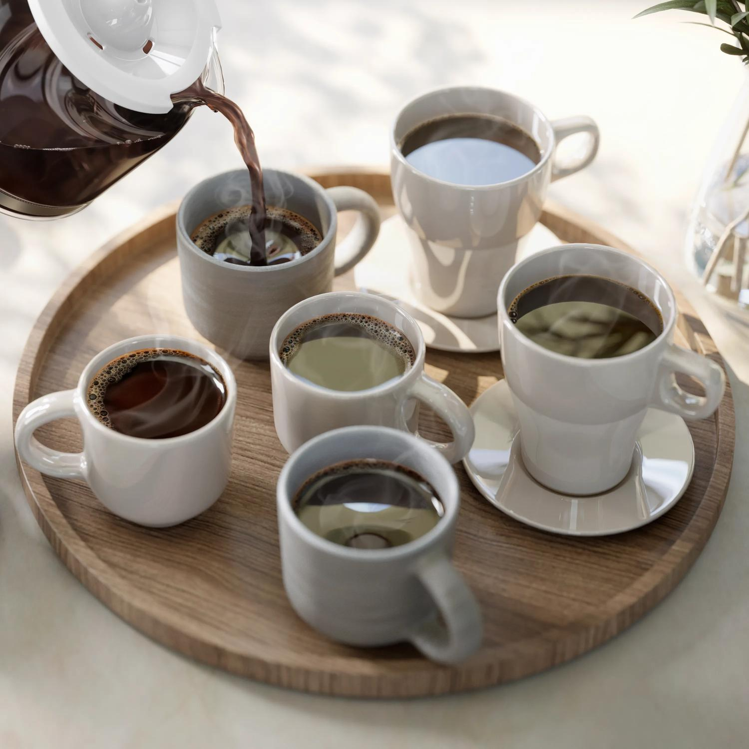 Kawa jest nalewana z dzbanka ze szkła do pięciu filiżanek na drewnianej tacy.