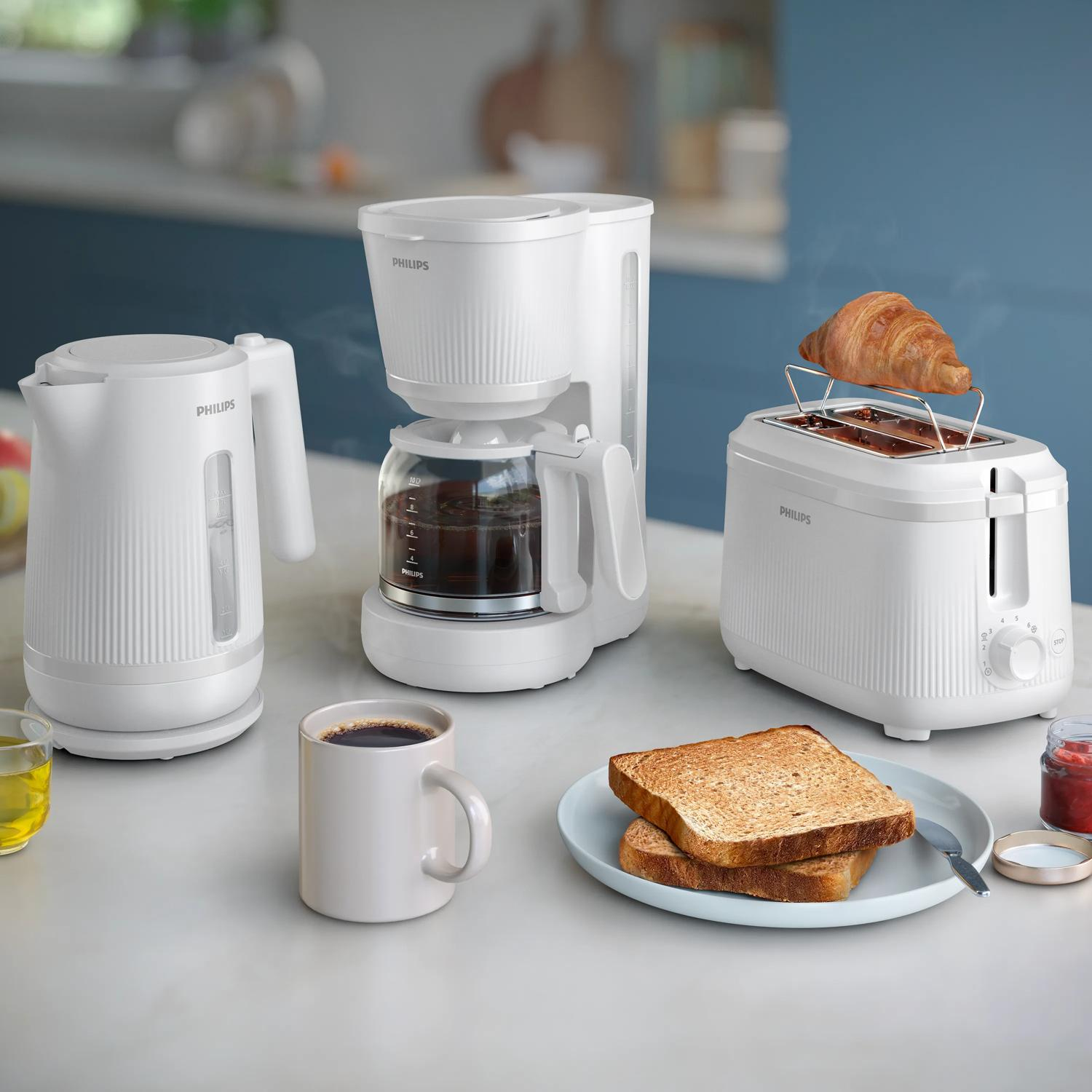 Biały czajnik, ekspres do kawy, toster z rogalikiem i tostem.