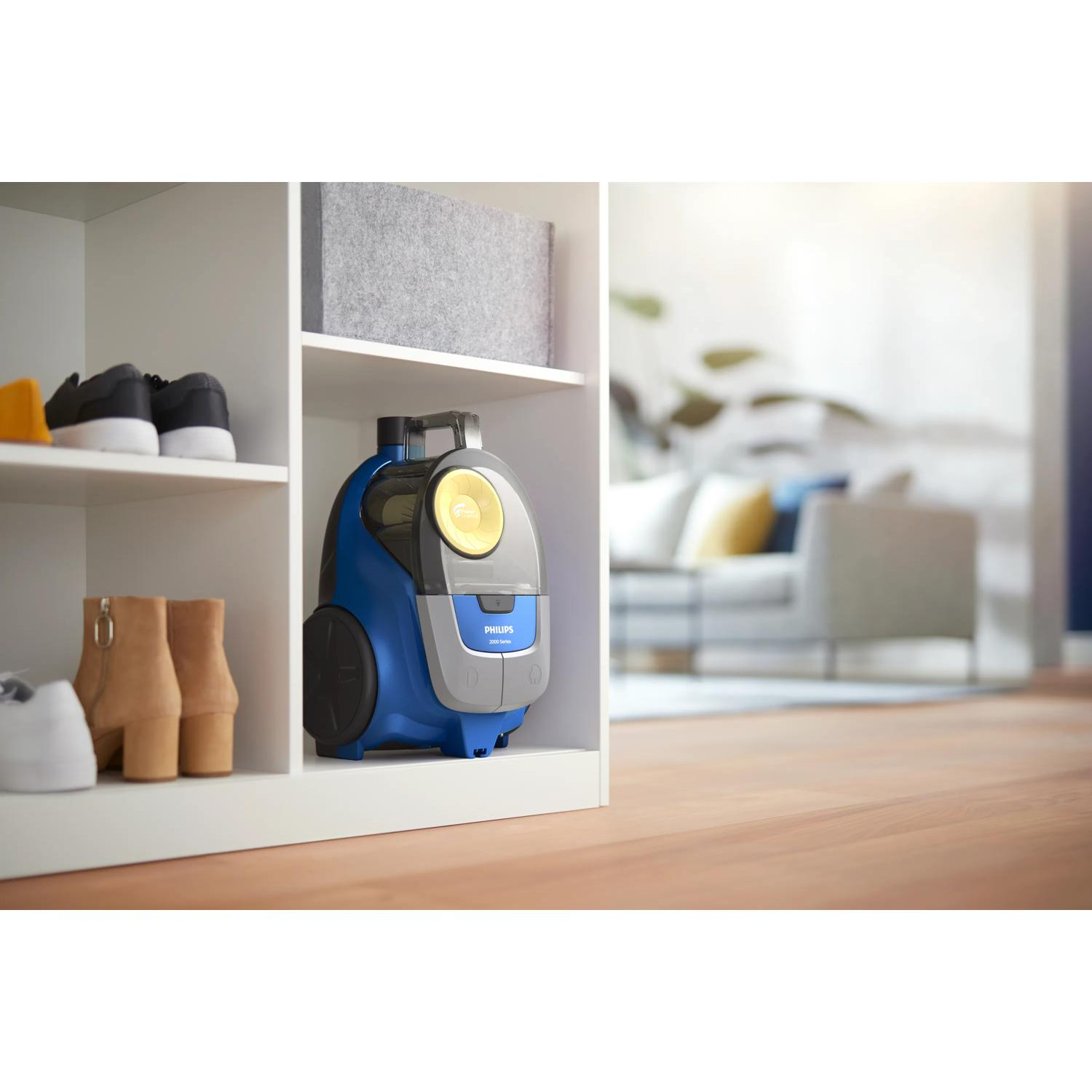 Blauwe Philips stofzuiger op plank met schoenen en grijze doos. Woonkamer.