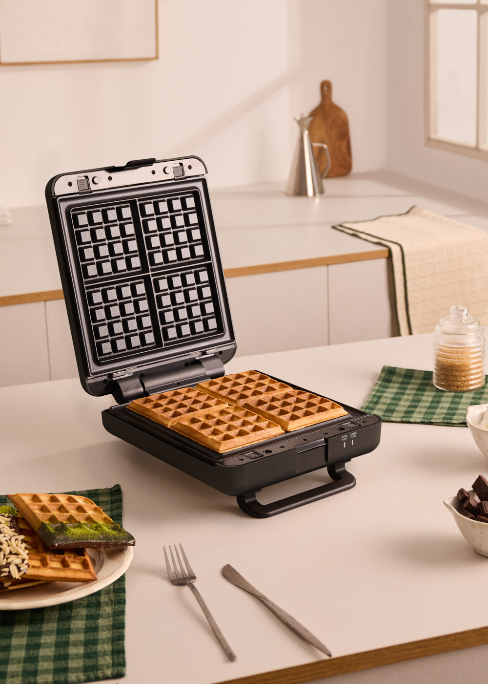 Gofre maker abierto con cuatro gofres dorados dentro. Cerca hay un plato con gofres.