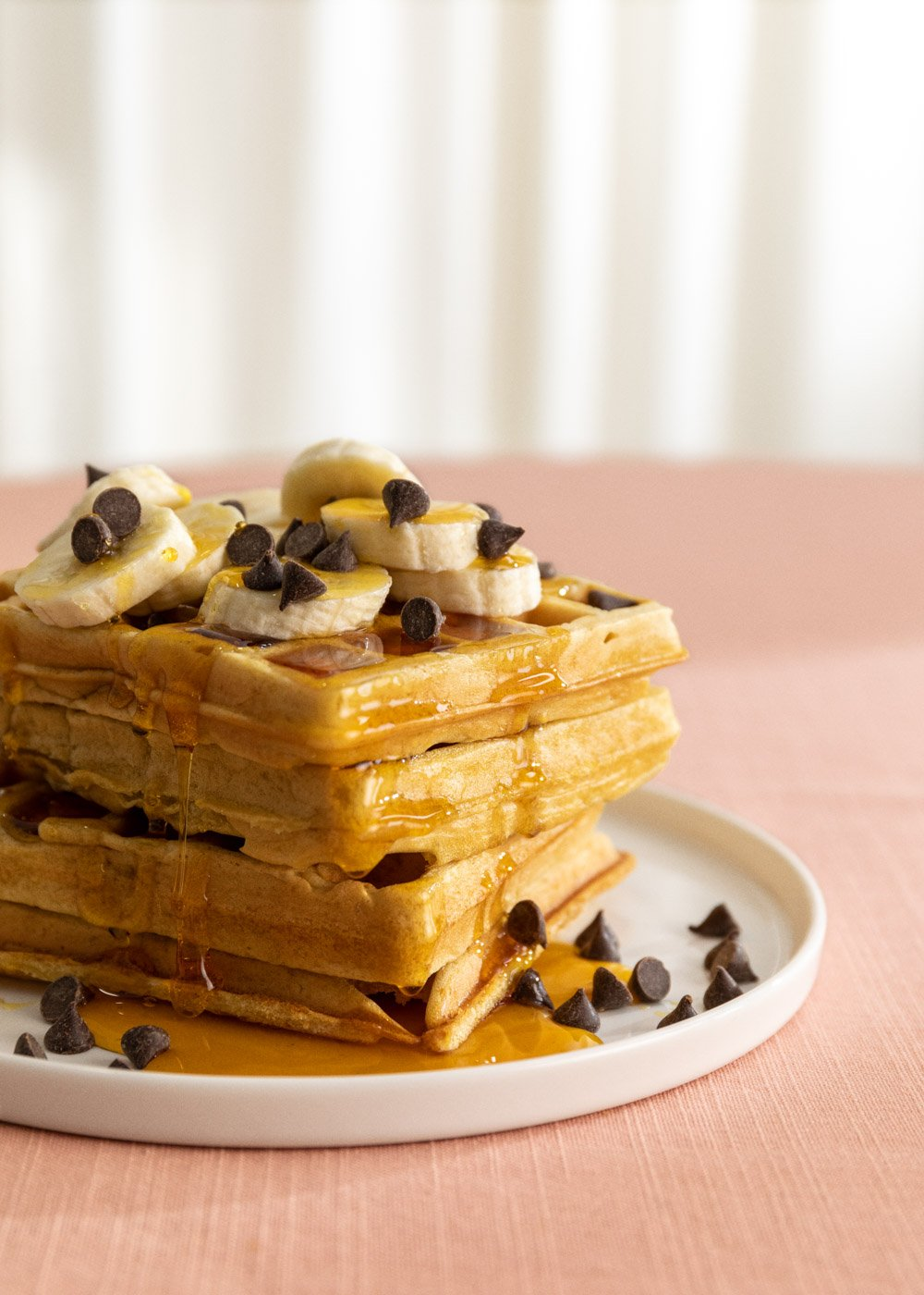 Una pila de gofres con rodajas de plátano, chispas de chocolate y sirope.