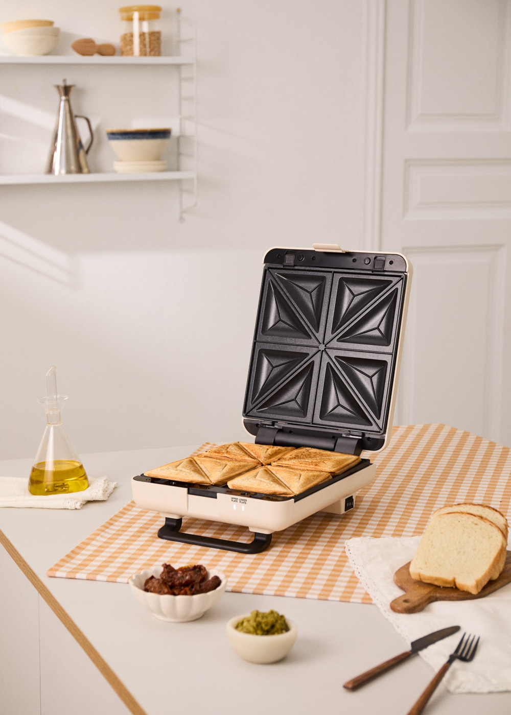 Una sandwichera abierta con cuatro sándwiches tostados, ingredientes y pan cerca.