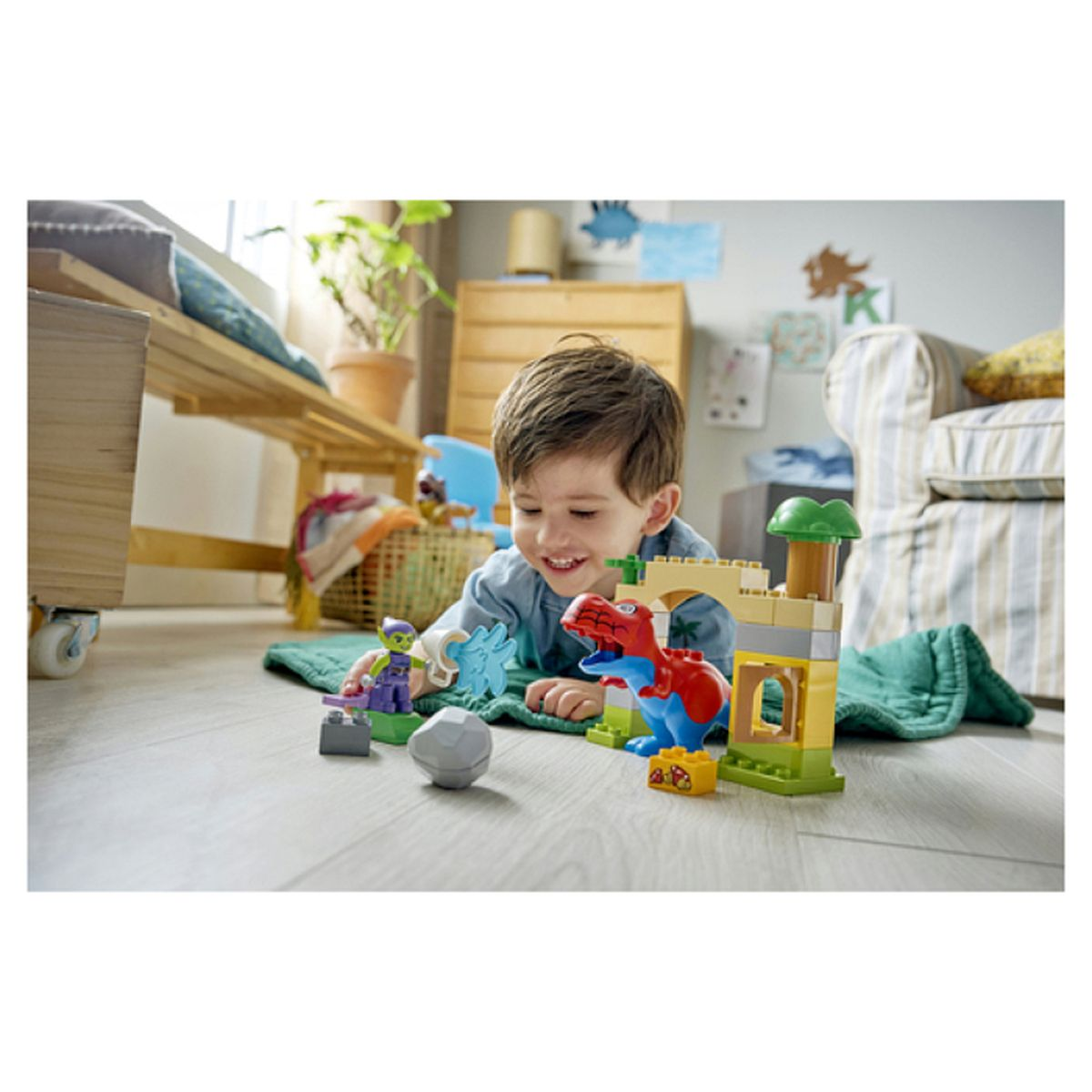 Chłopiec bawi się klockami Lego - dinozaurami i figurkami na podłodze.