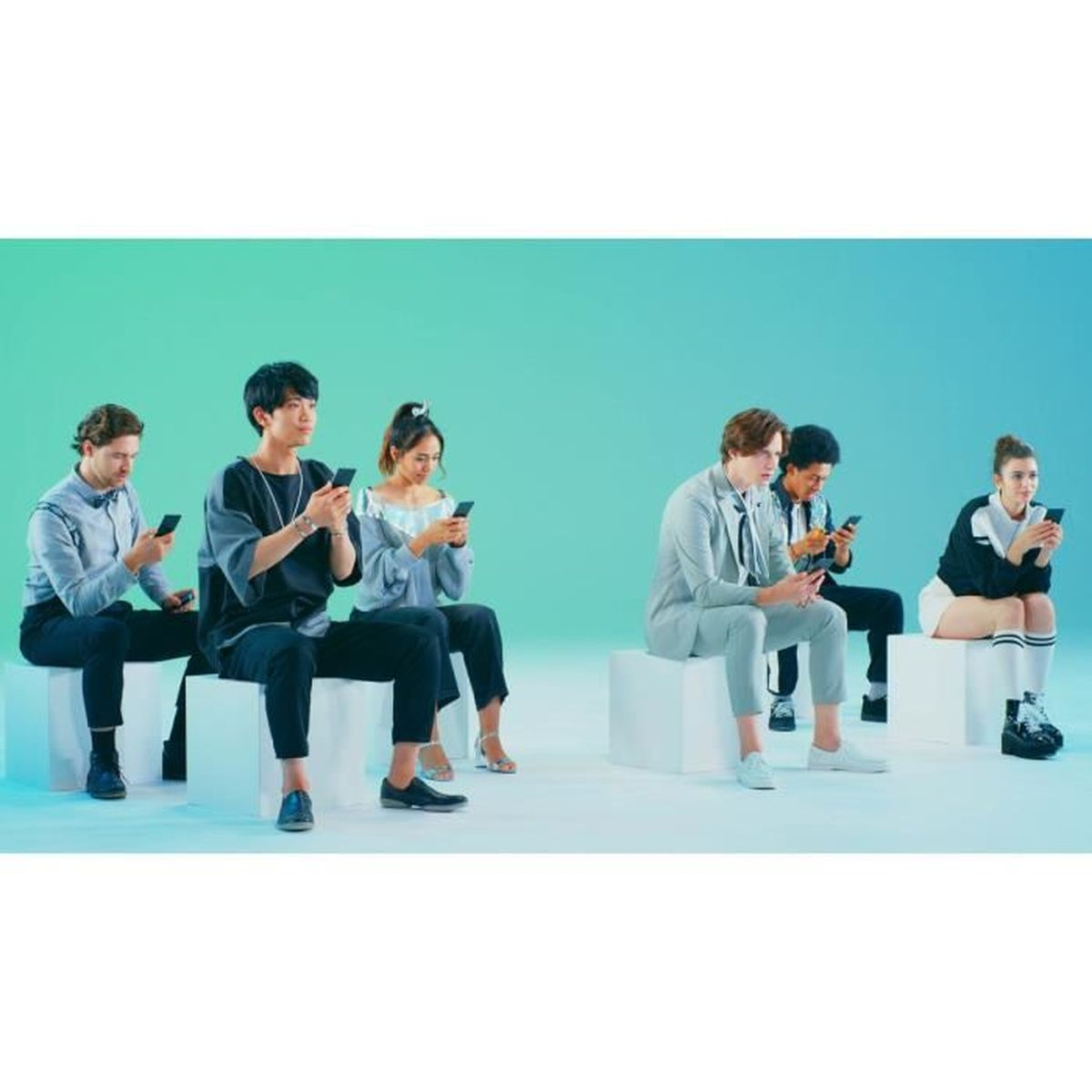 Sei giovani siedono su cubi bianchi, guardando i loro telefoni.