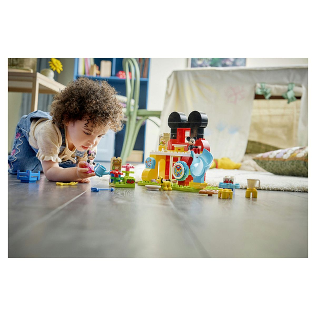 Maluch bawi się kolorowymi figurkami Lego przed domkiem do zabawy.