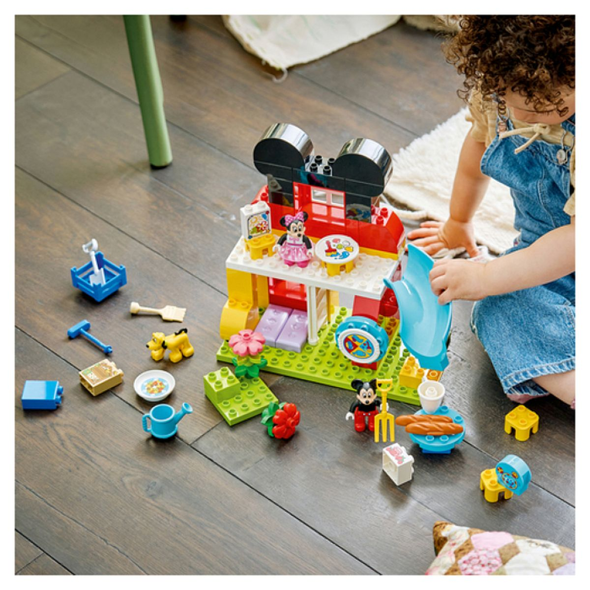 Dziecko bawi się zestawem Lego Myszki Miki na drewnianej podłodze. Widoczni Myszka Miki i Minnie.